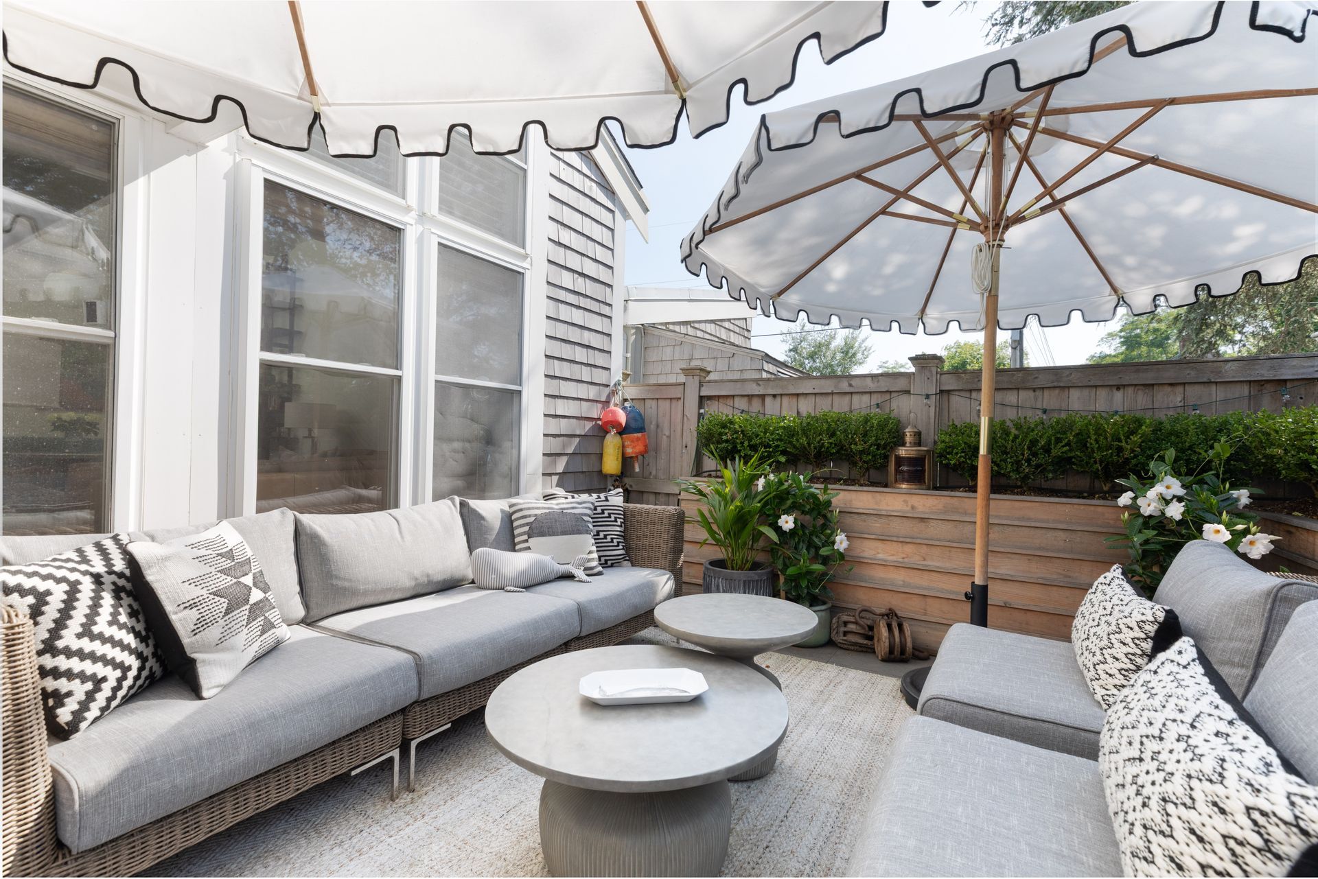 Covered patio with gray sofas, round coffee table, patterned cushions, and large umbrellas.