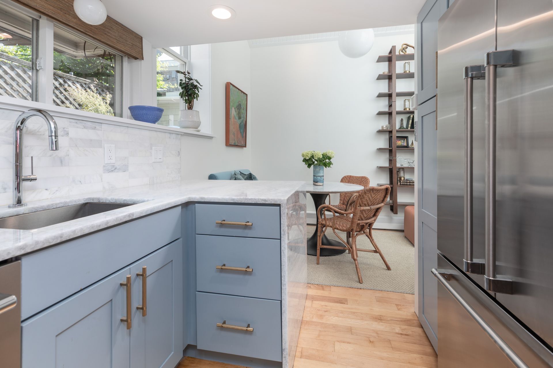 Bright modern kitchen with blue cabinets, white tile backsplash, and stainless steel refrigerator leading to a dining area