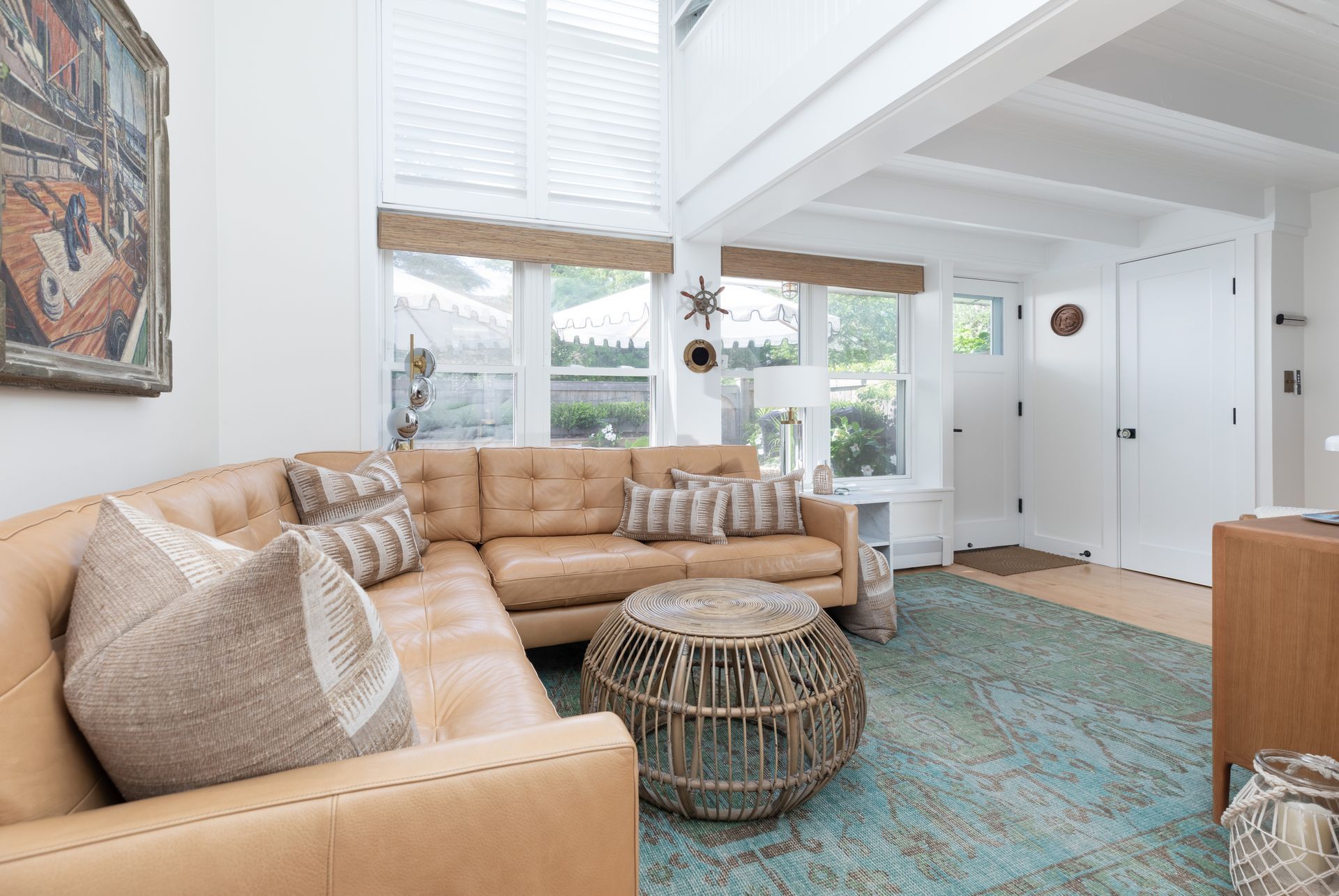 Bright living room with tan sectional, patterned rug, wicker coffee table, and large windows.