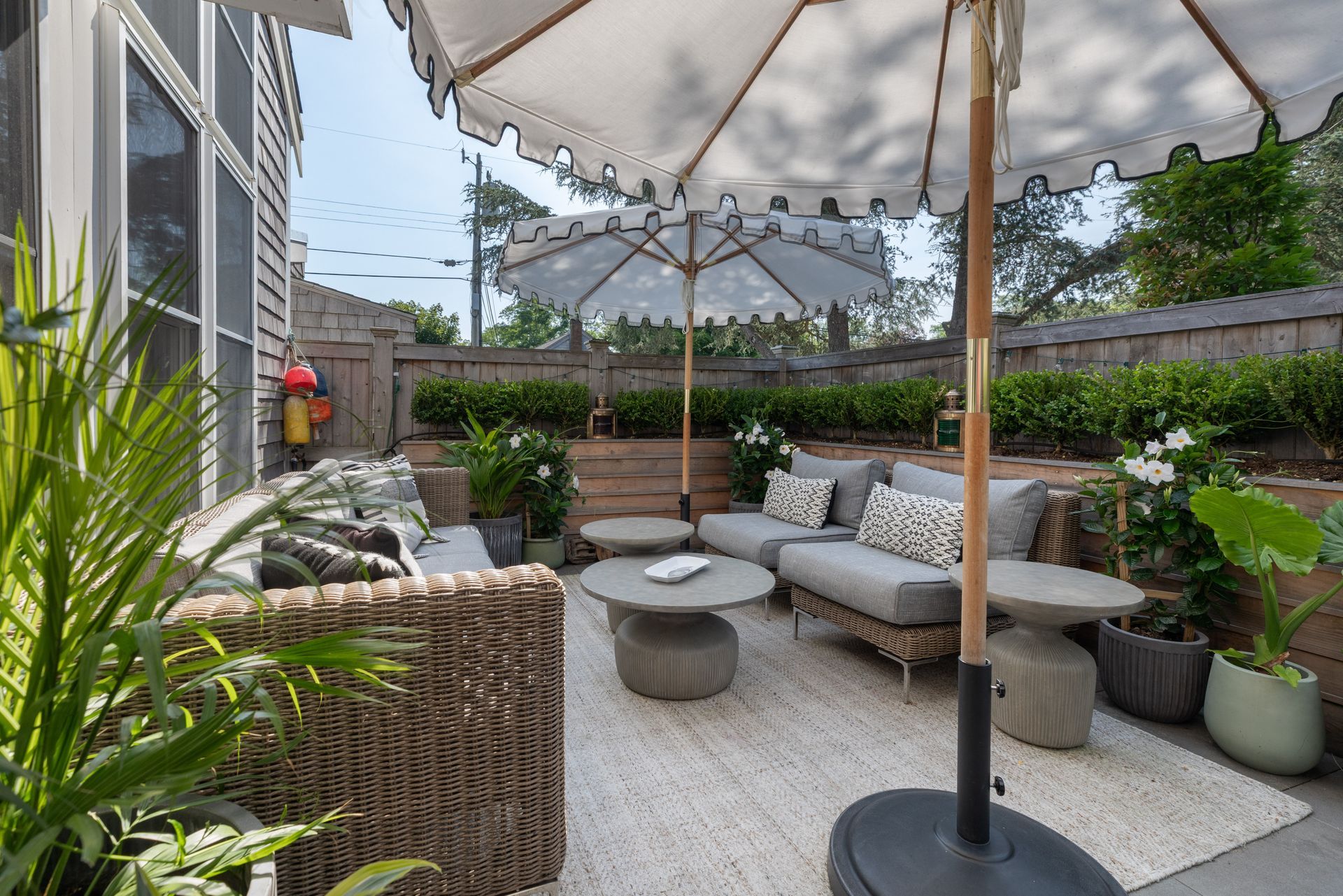Patio seating area with white umbrella, woven chairs, round tables, and potted plants beside a house