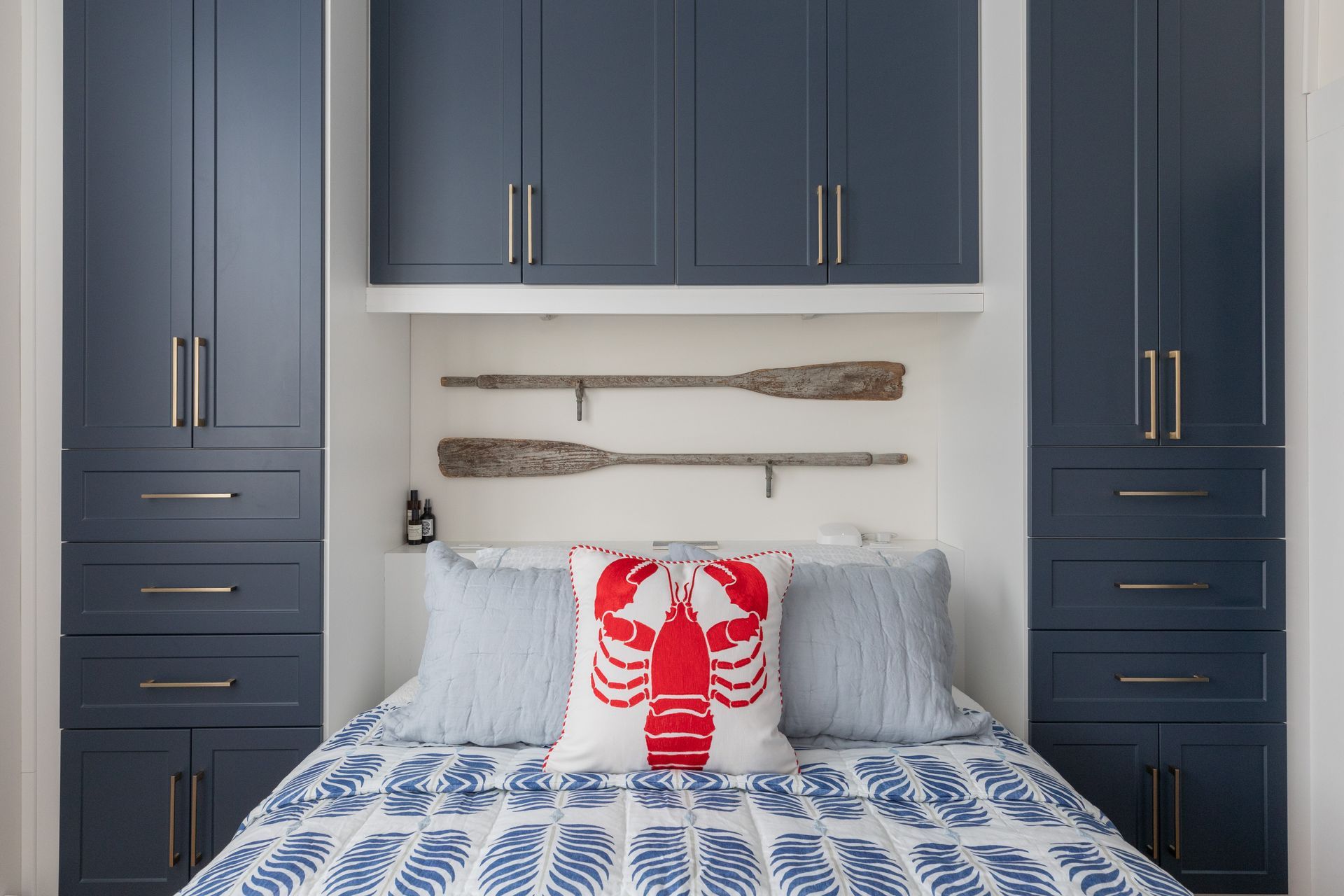 Blue bedroom with built-in cabinets, white shiplap wall, and a bed with blue-patterned bedding and a red lobst er pillow