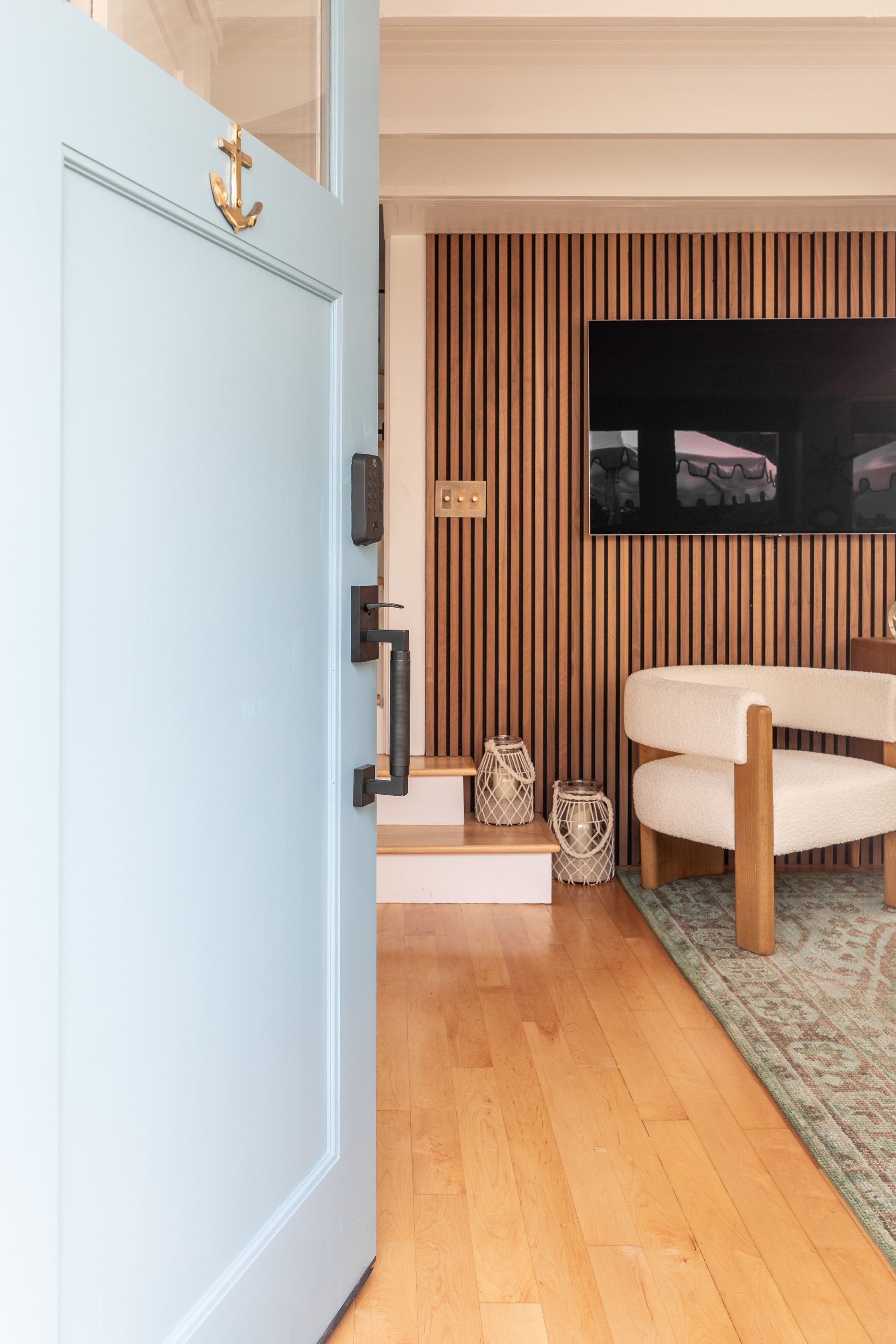 Open blue front door with a view into a warm, modern living room with wood slat wall and beige chair