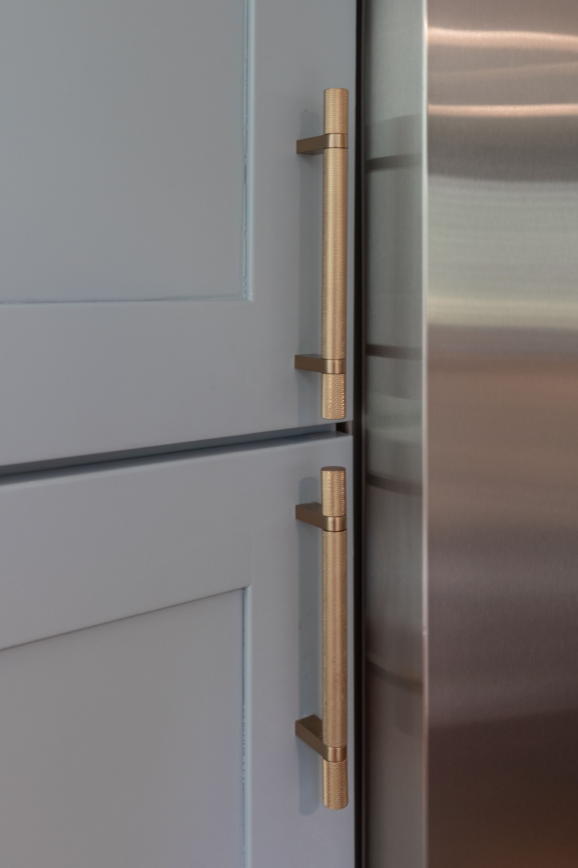 Close-up of gold cabinet pulls on a light gray door beside a stainless steel appliance