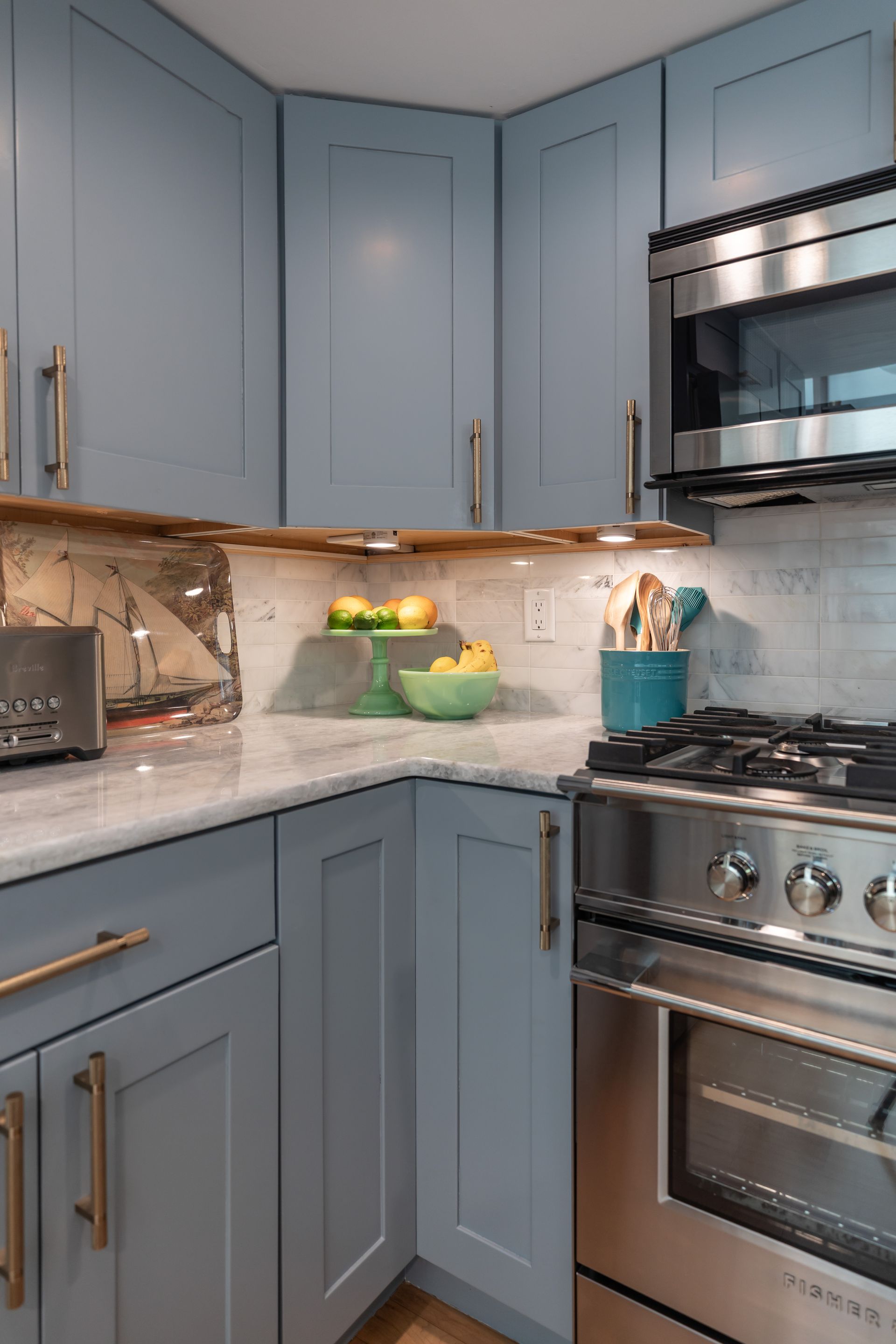 Blue-gray kitchen with marble counters, gas stove, and a bowl of fruit on the counter