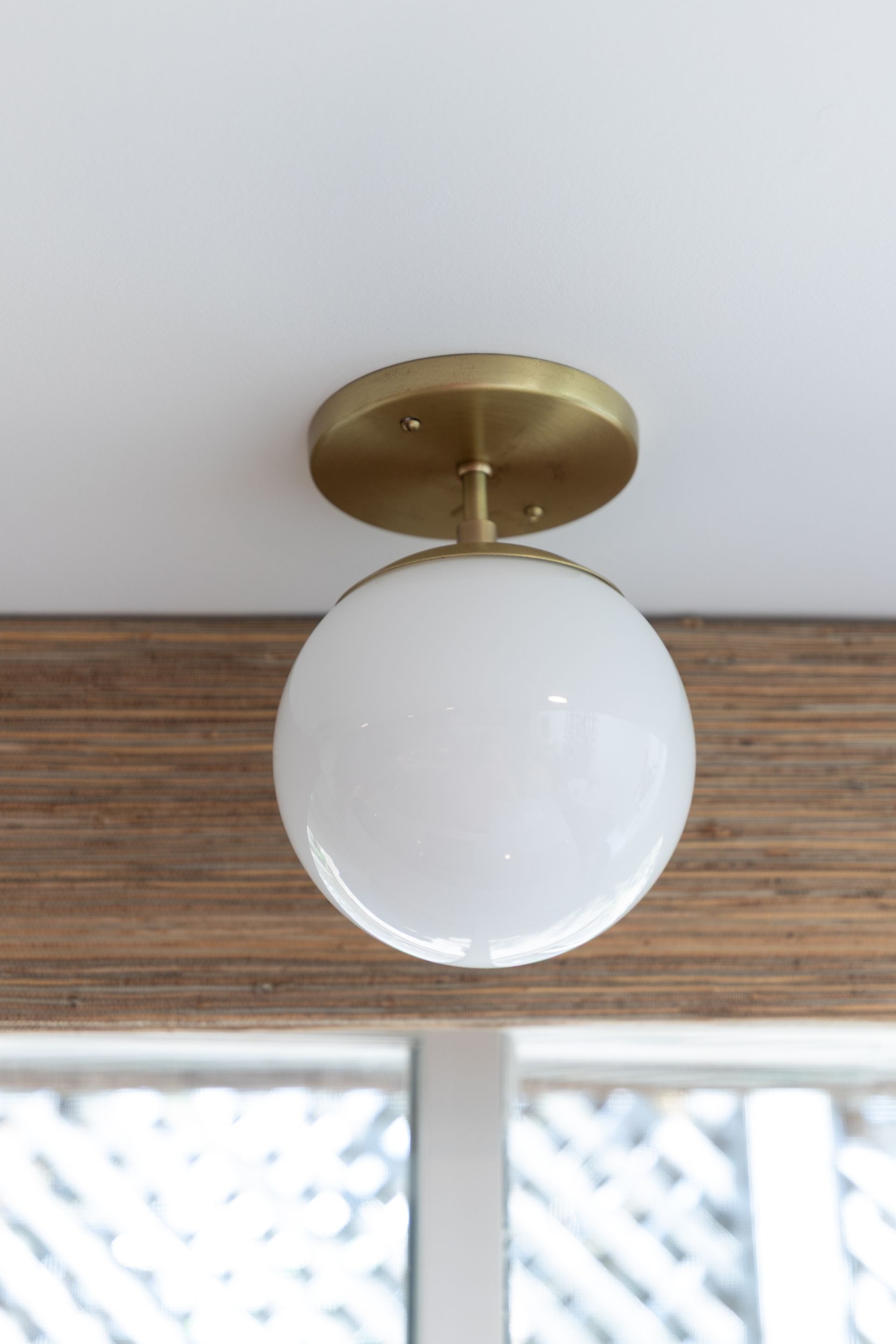 Brass ceiling fixture with a white globe shade on a white ceiling above a window frame