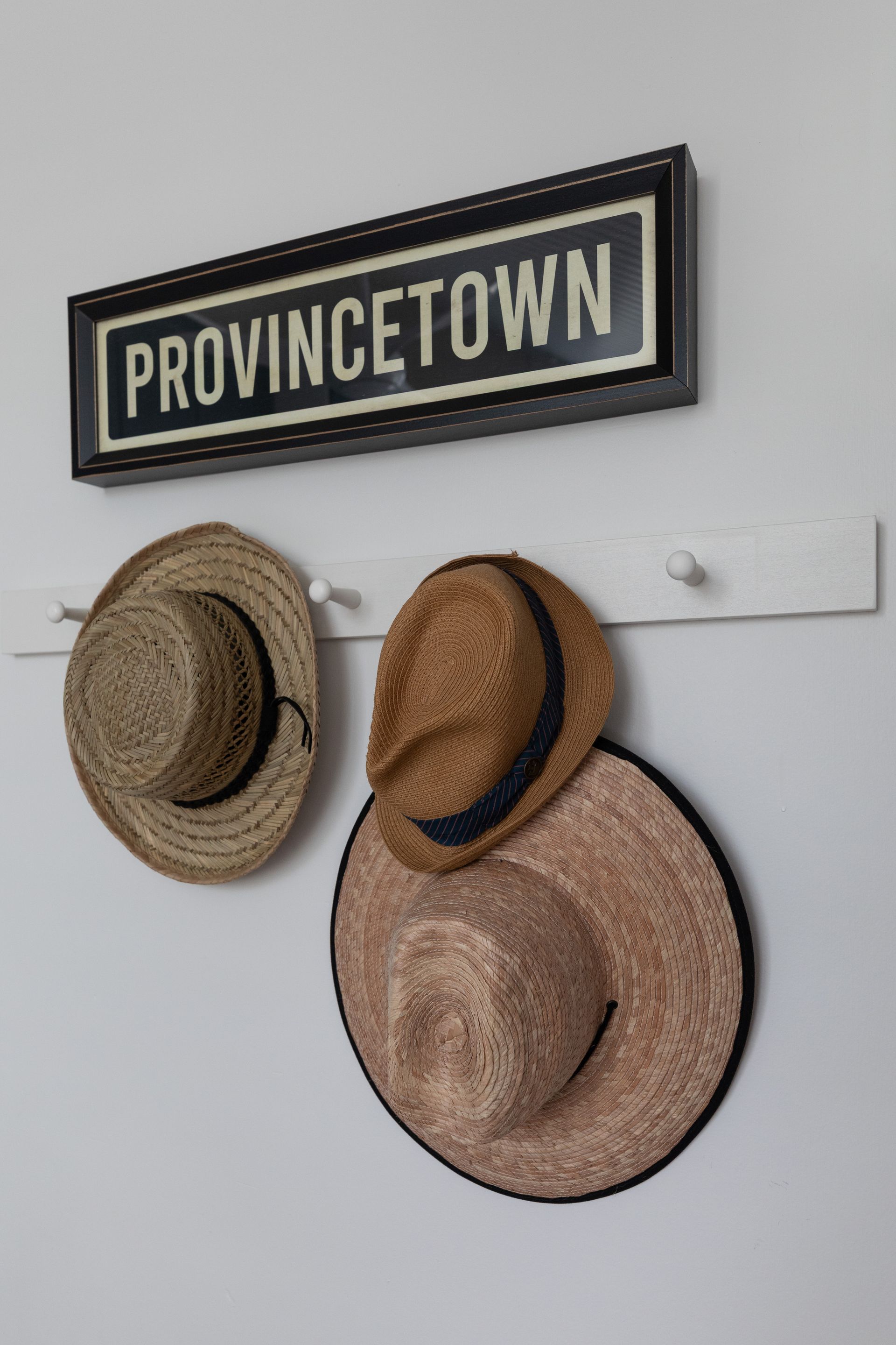 Provincetown sign above three straw hats hanging on a white wall