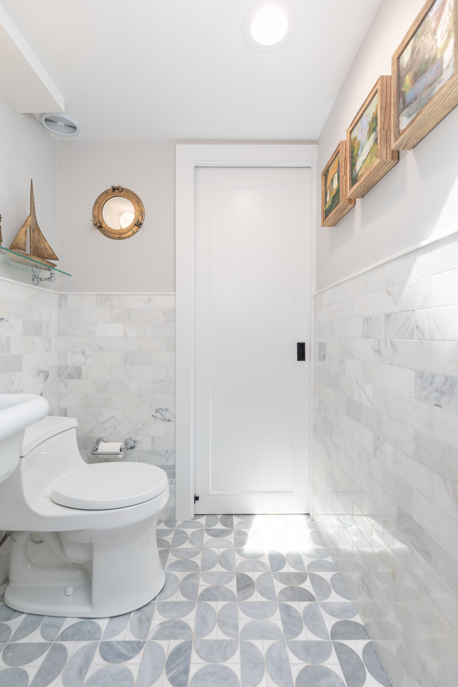 Bright bathroom with toilet, patterned tile floor, white door, and framed wall art