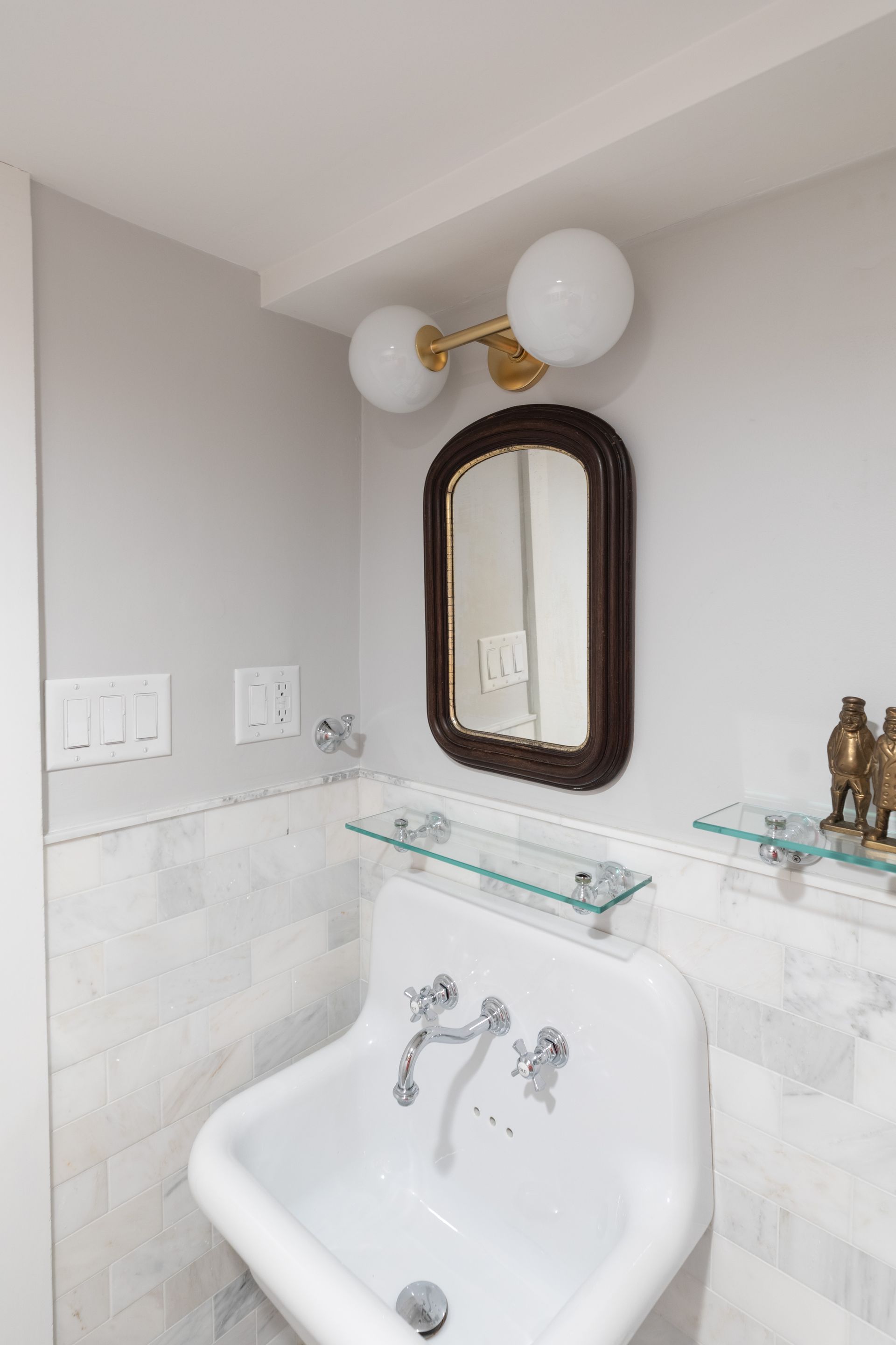 Small bathroom corner with pedestal sink, mirror, and brass light fixture over marble tile walls
