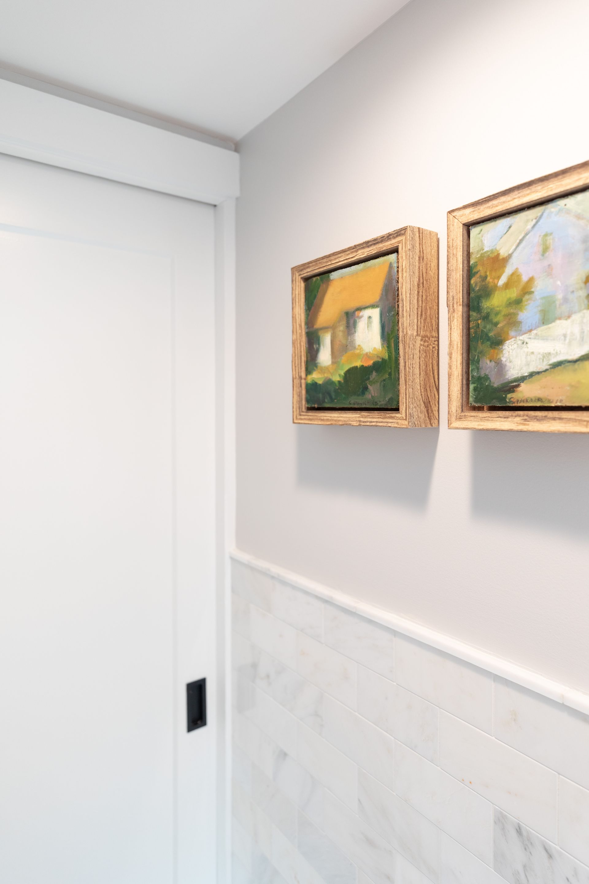 Hallway wall with two framed landscape paintings beside a white sliding door