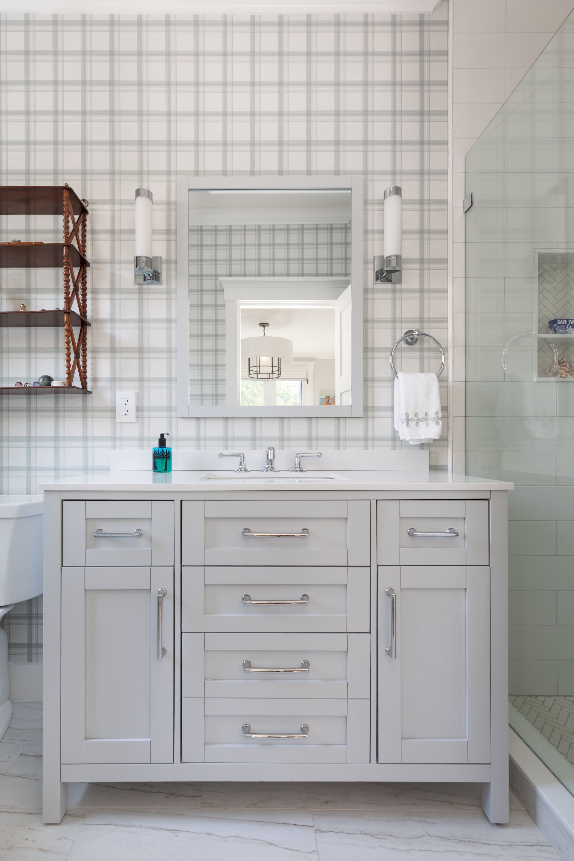 White bathroom vanity with mirror, wall sconces, and glass shower enclosure in a bright tiled bathroom