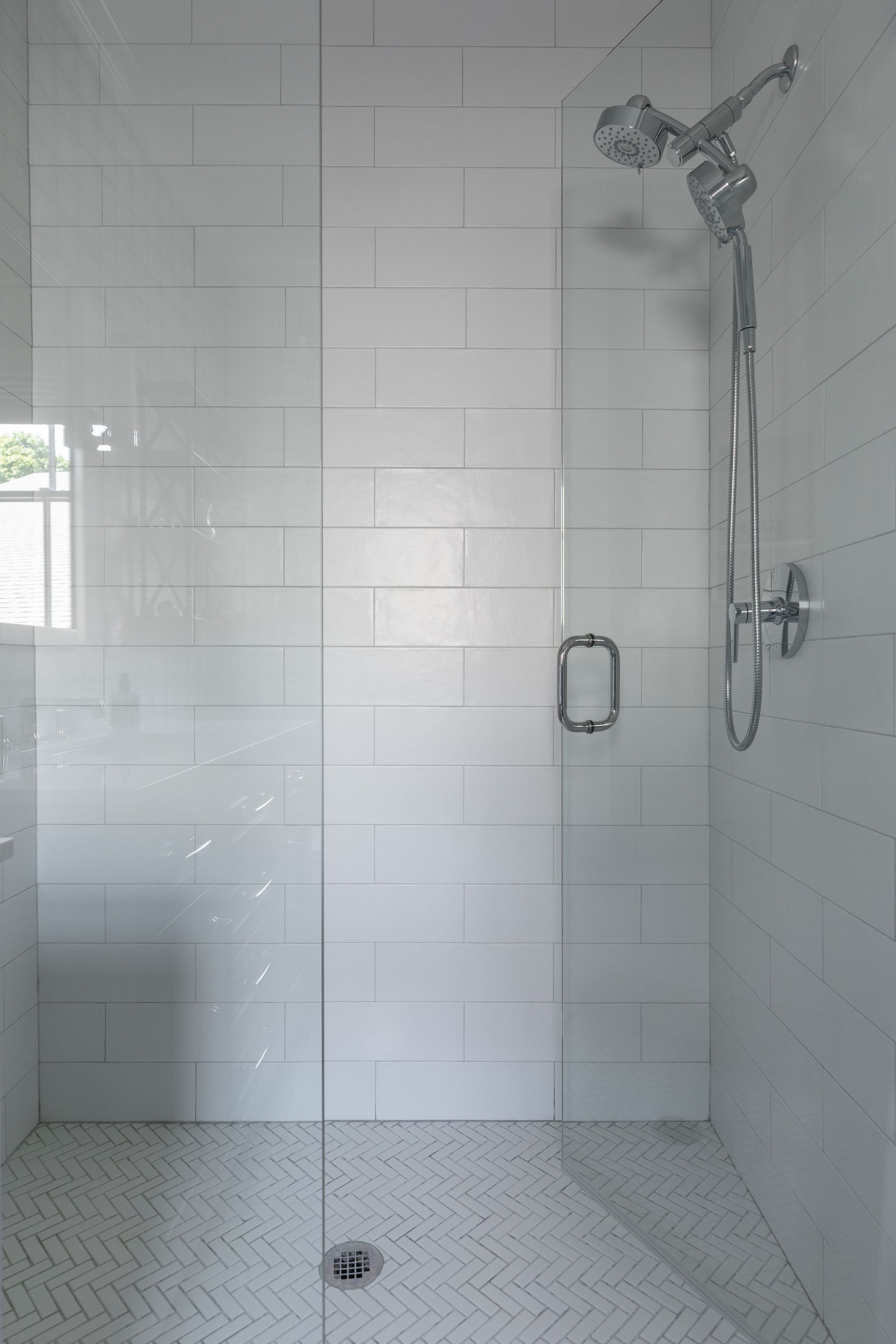 Walk-in shower with white tile, chrome showerhead, grab bar, and bench seat.