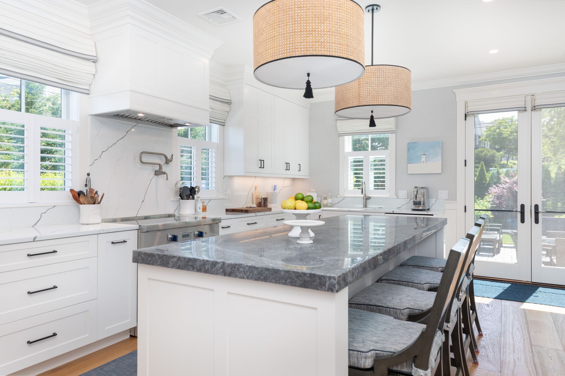 Bright white kitchen with marble island, woven pendant lights, and bar stools by large windows