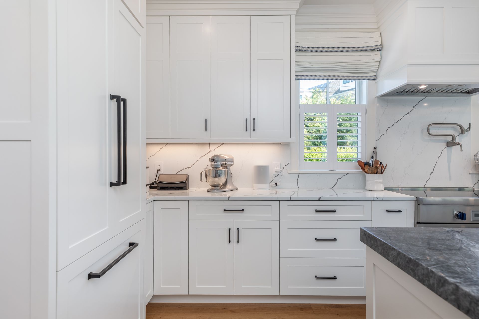 Bright white kitchen with cabinets, dark countertops, and a window above the sink