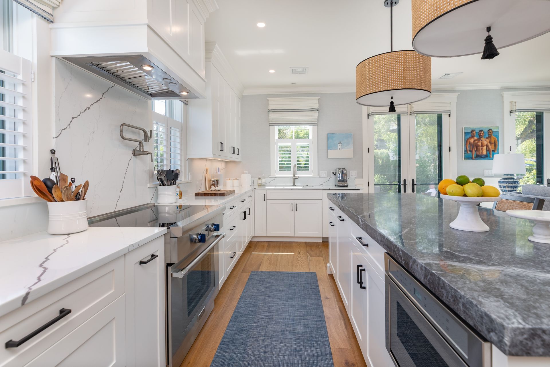 Bright white galley kitchen with gray countertops, blue runner, and a fruit bowl on the island.