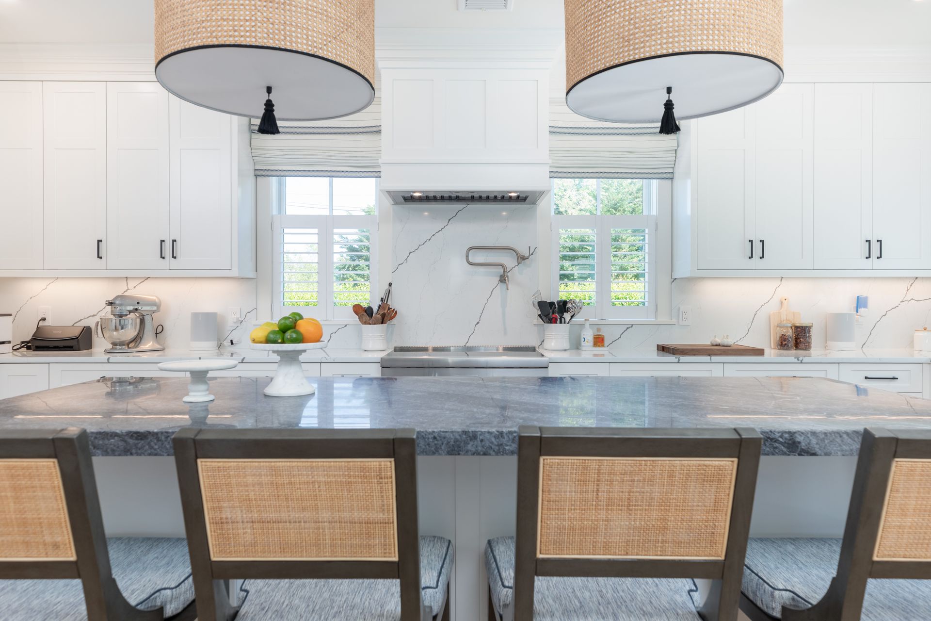 Bright modern kitchen with blue island, wicker stools, white cabinets, and pendant lights