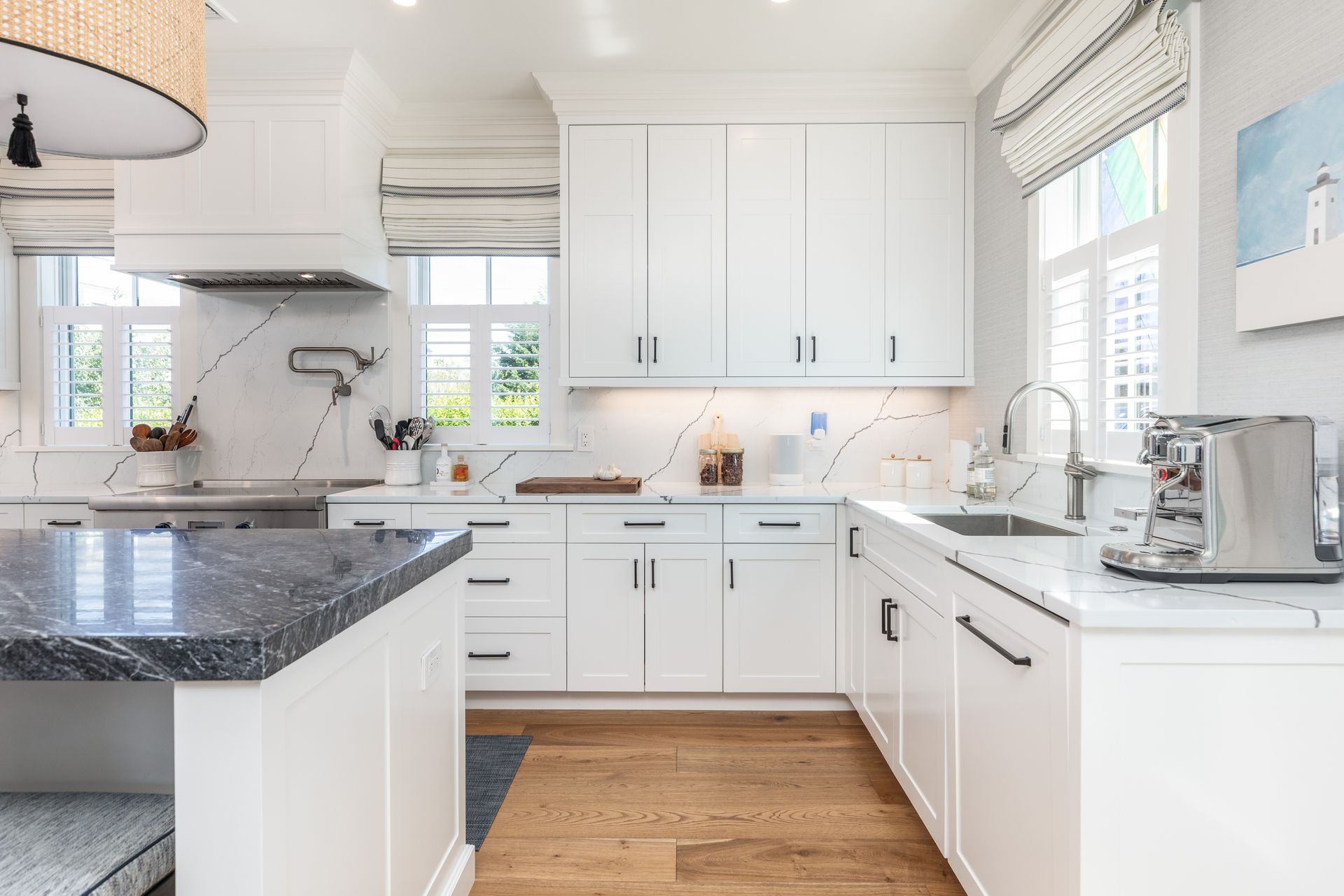 Bright white kitchen with marble counters, island, wooden floor, and a window over the sink.