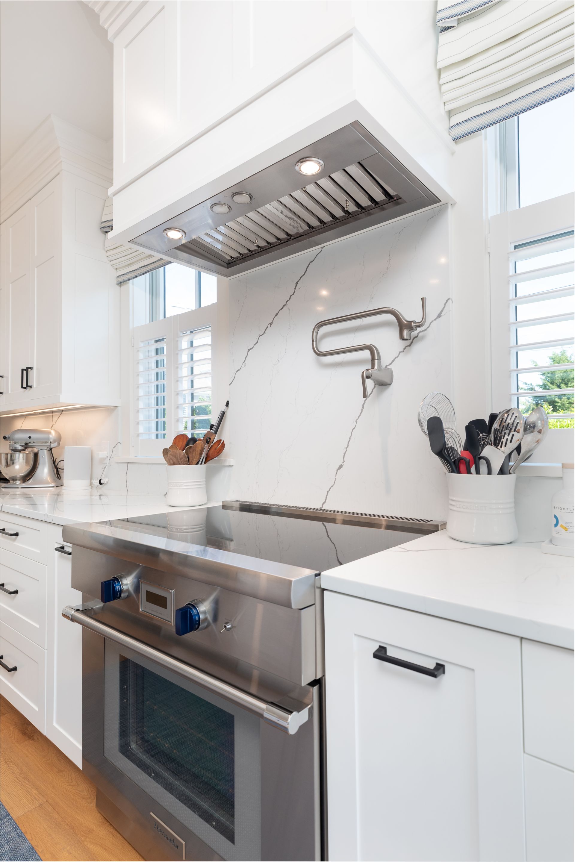 Bright white kitchen with stainless steel stove, range hood, sink, and marble backsplash