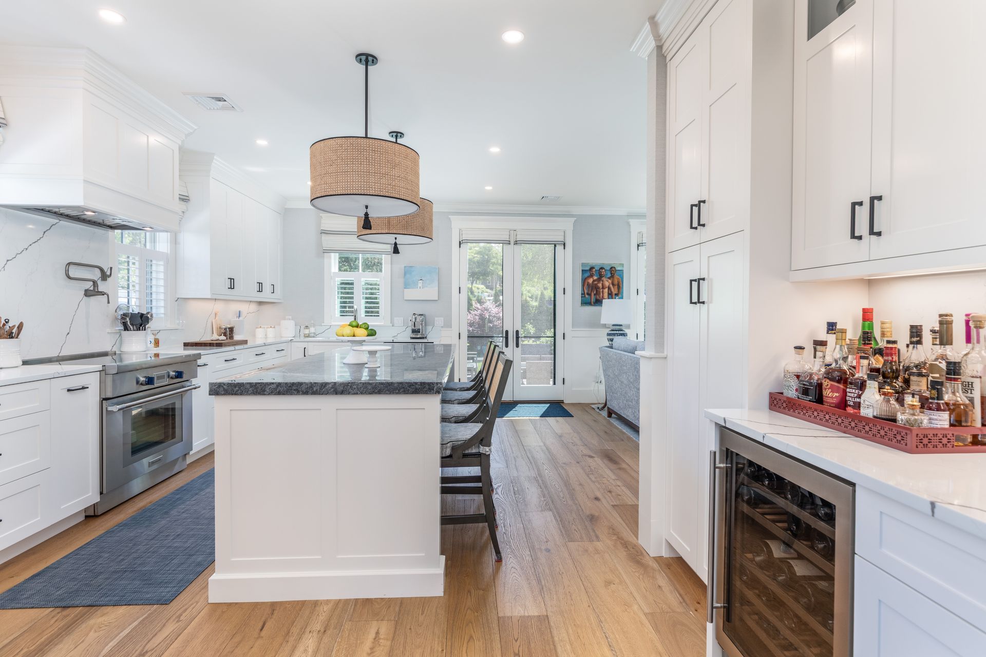 Bright modern kitchen with white cabinets, island, hardwood floors, and a small breakfast nook by glass doors