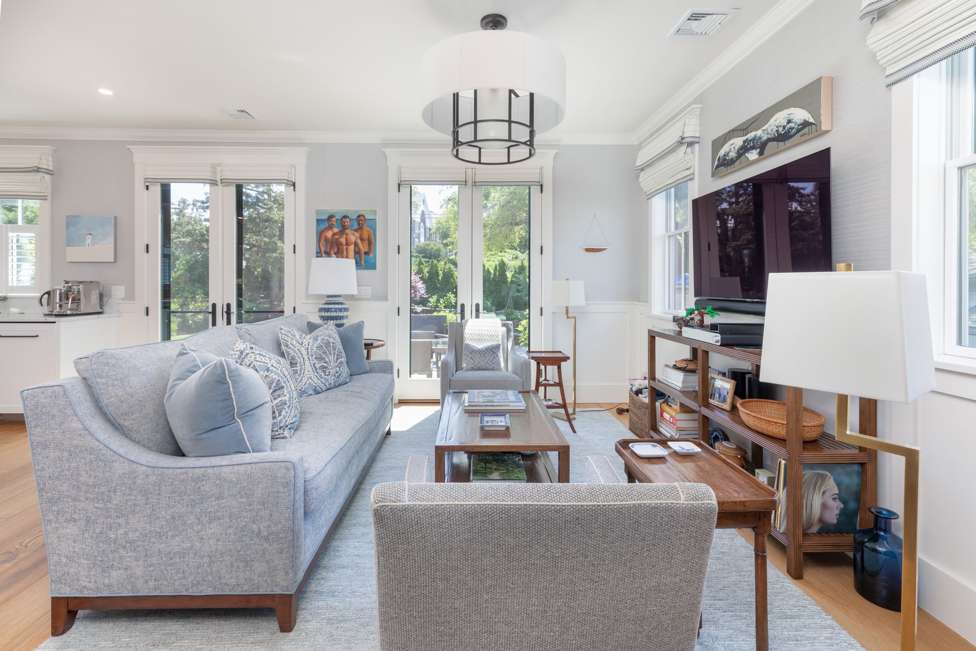 Bright living room with gray sofas, a coffee table, large TV, and tall windows letting in natural light