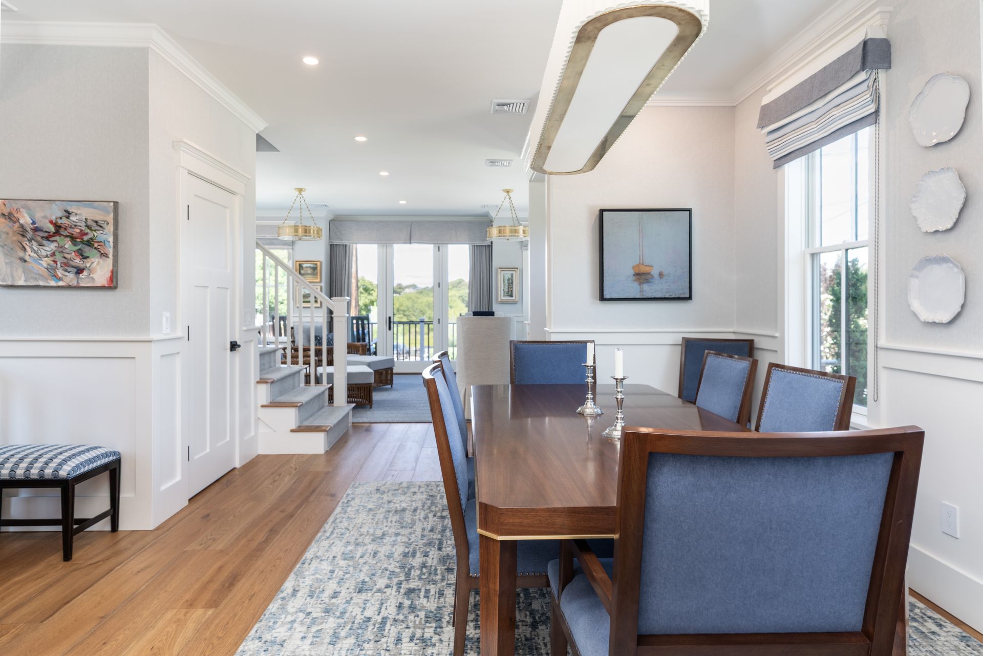 Bright dining room with wooden table, blue chairs, white walls, and a view into a sunlit living area.