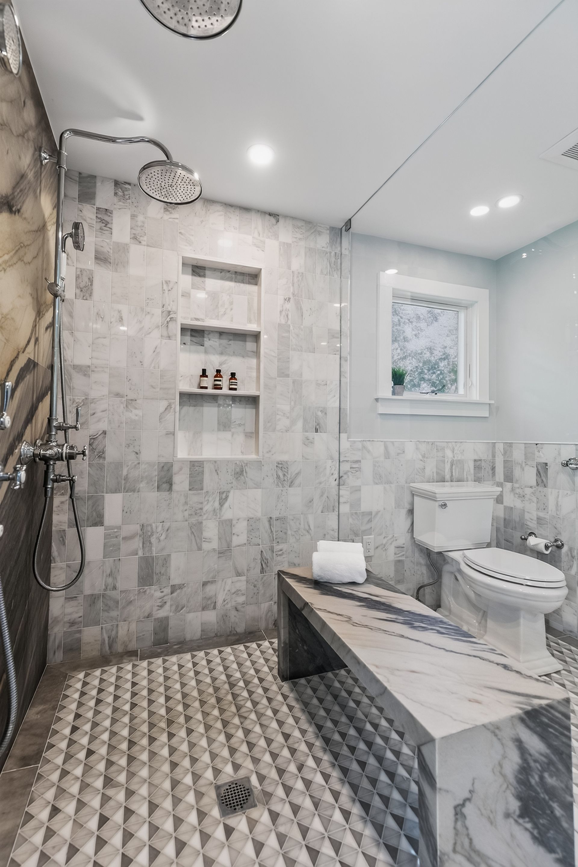 Modern gray marble bathroom with walk-in shower, window, and freestanding tub with patterned floor