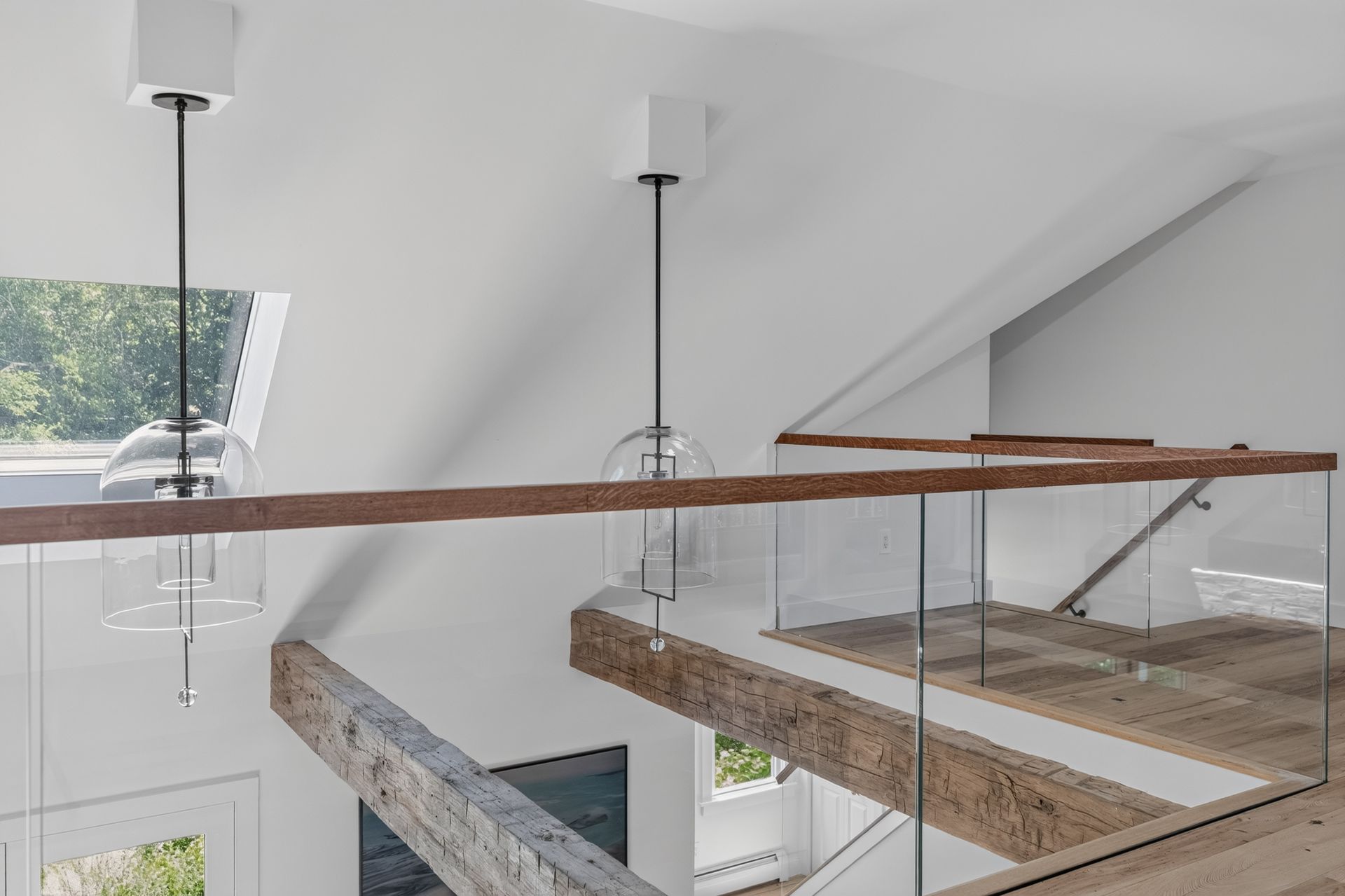 Modern loft interior with hanging pendant lights, skylights, and exposed wood beams along a mezzanine corridor