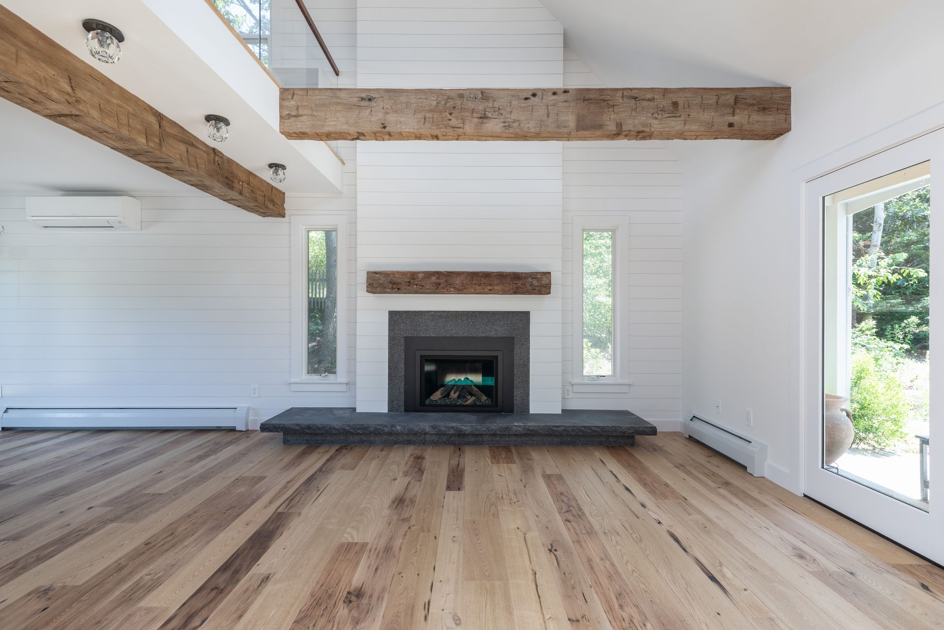 Bright modern living room with hardwood floors, white walls, exposed beams, and a fireplace.