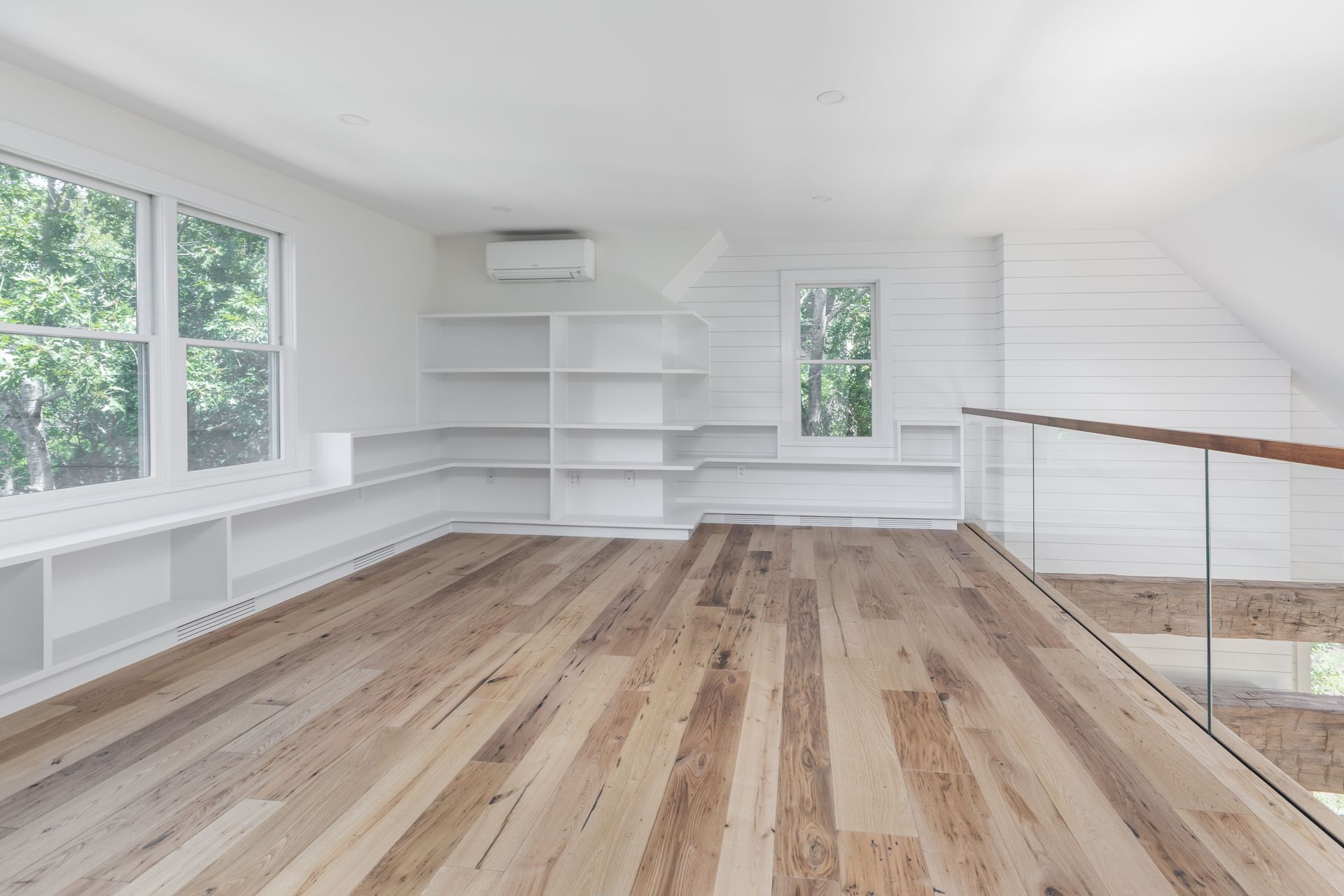 Bright empty room with white built-in shelves, large windows, and light wood floors