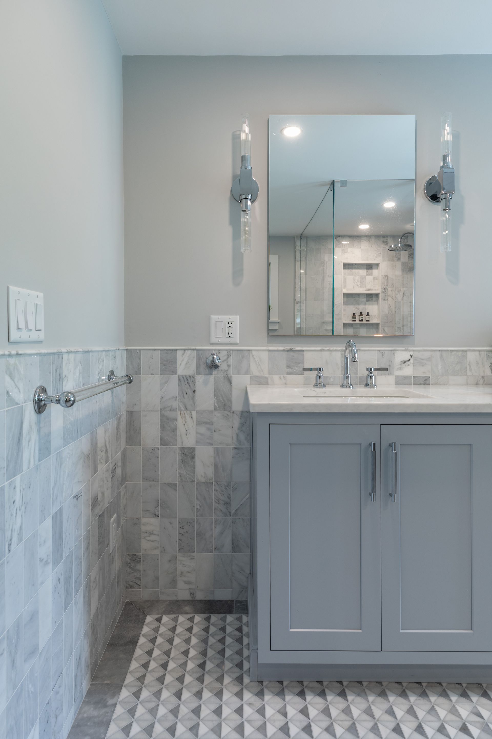 Small bathroom with gray vanity, marble countertop, mirror, and patterned tile walls and floor.