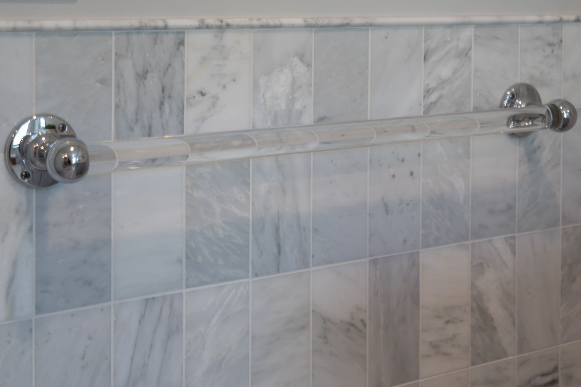 Chrome towel bar mounted on a light gray tiled bathroom wall