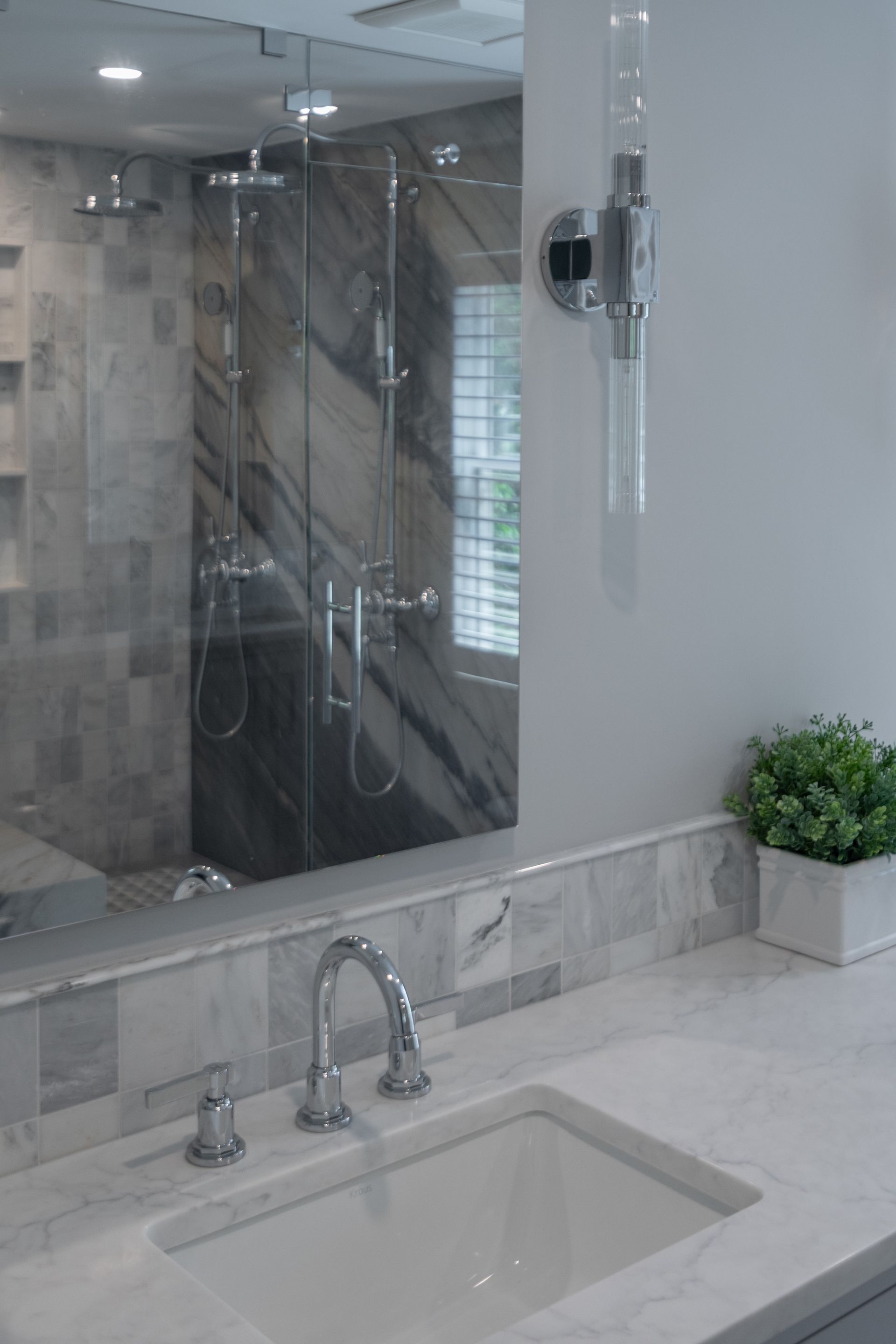 Bathroom vanity with sink and chrome faucet, mirror wall, and shower visible in the background.