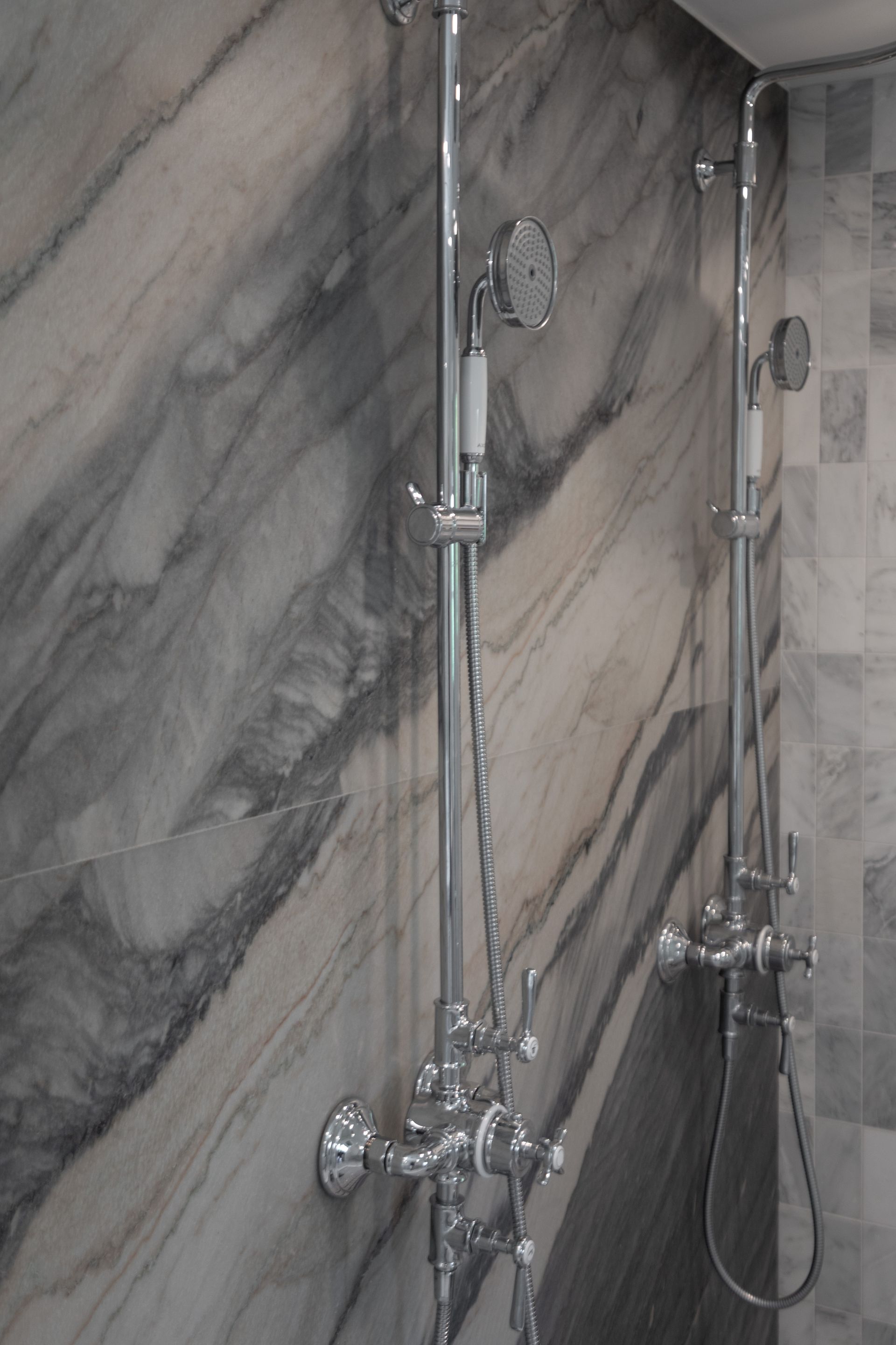 Marble shower wall with two chrome showerheads and handheld sprayers