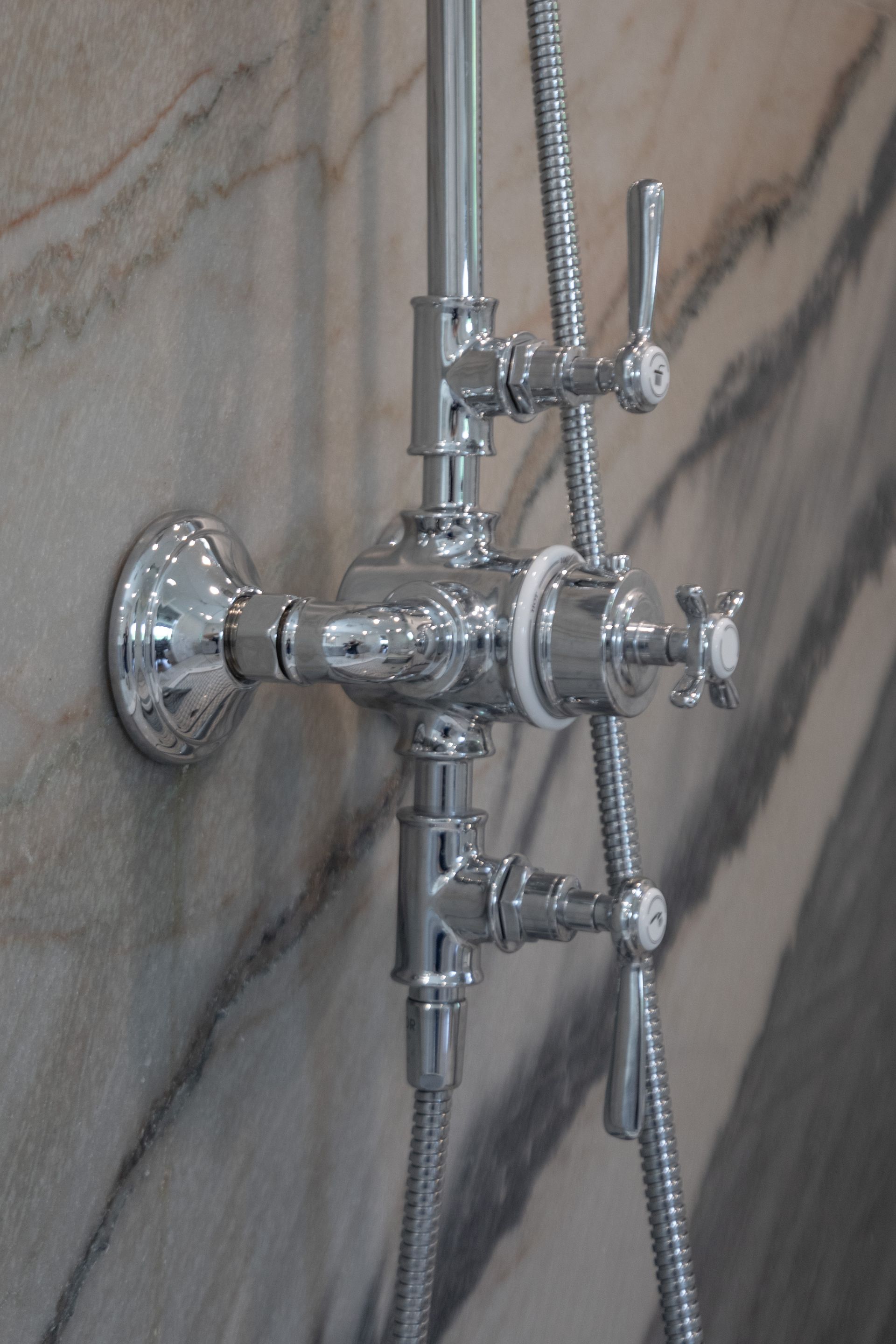 Chrome shower controls with handheld shower hose on a tiled bathroom wall