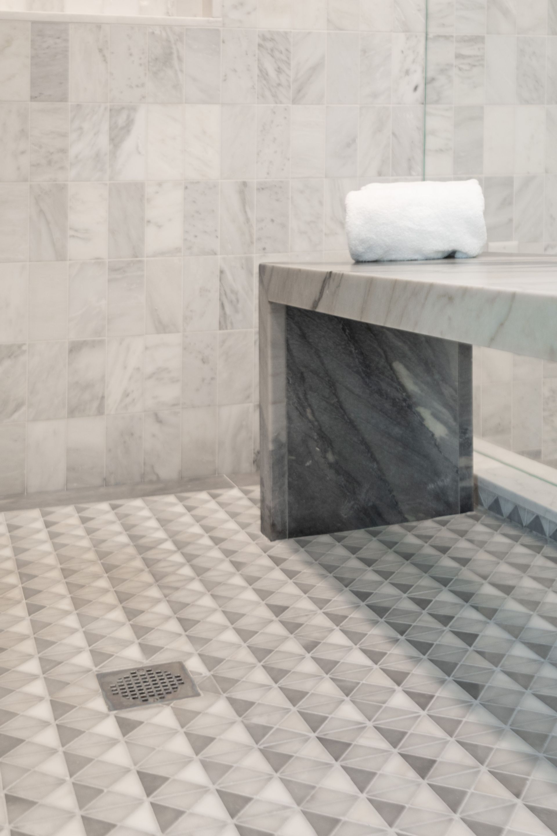 Modern tiled bathroom with a stone bench and folded white towel on top.