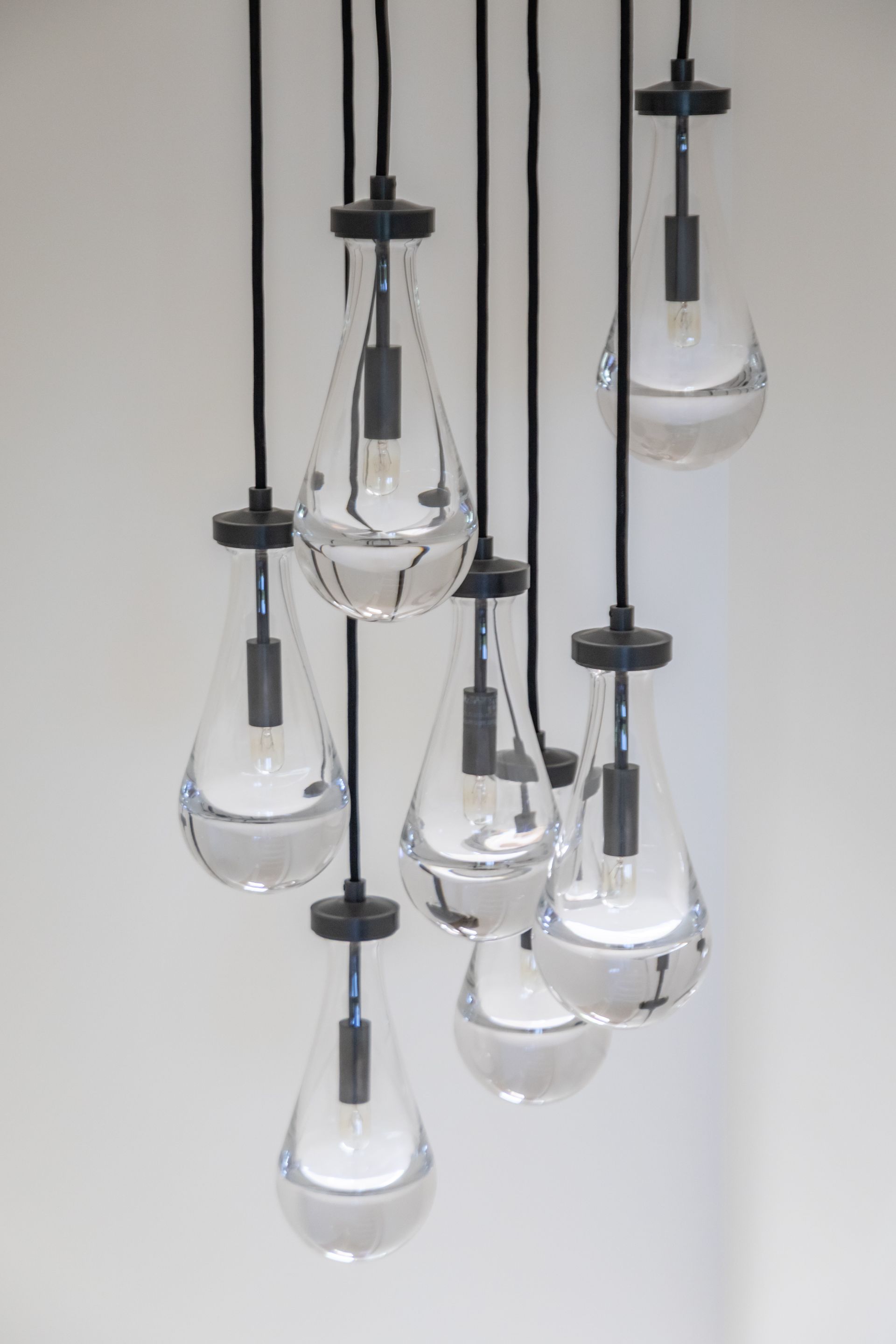 Cluster of hanging clear glass pendant lights against a plain white wall.
