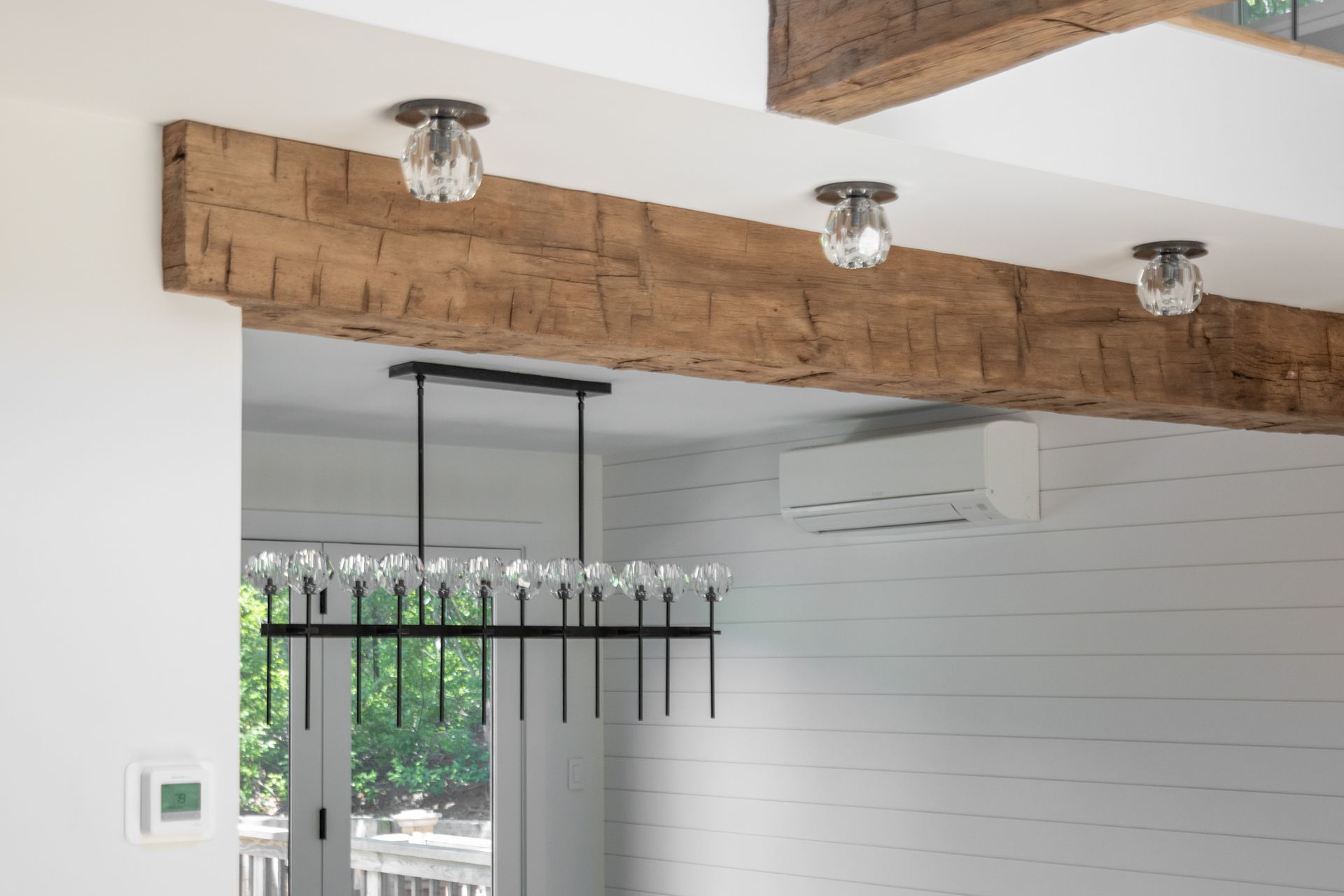 Interior with exposed wood beams, track lights, and a black hanging chandelier near a white shiplap wall.
