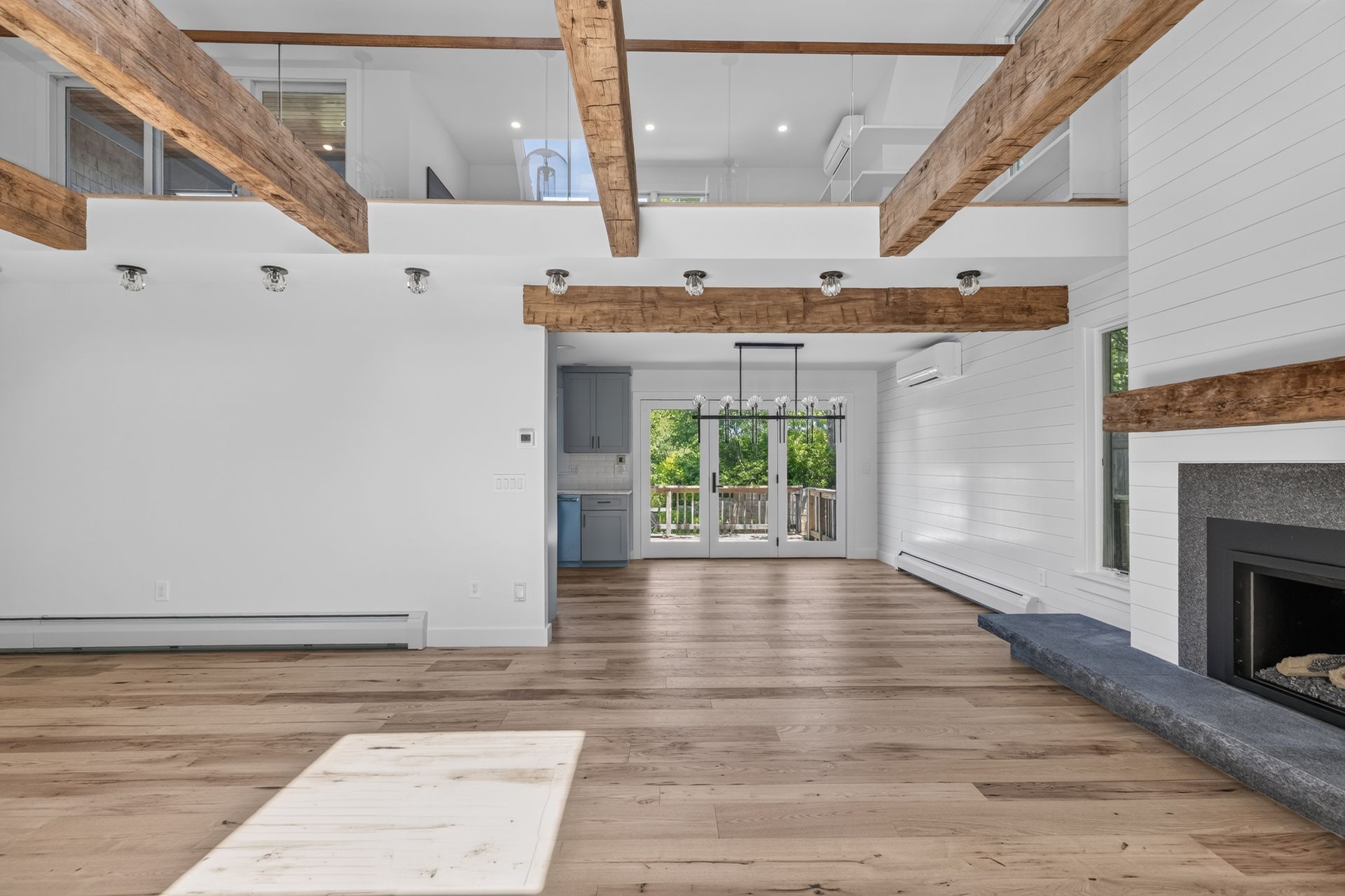 Spacious modern living room with exposed beams, wood floors, white walls, and a fireplace.