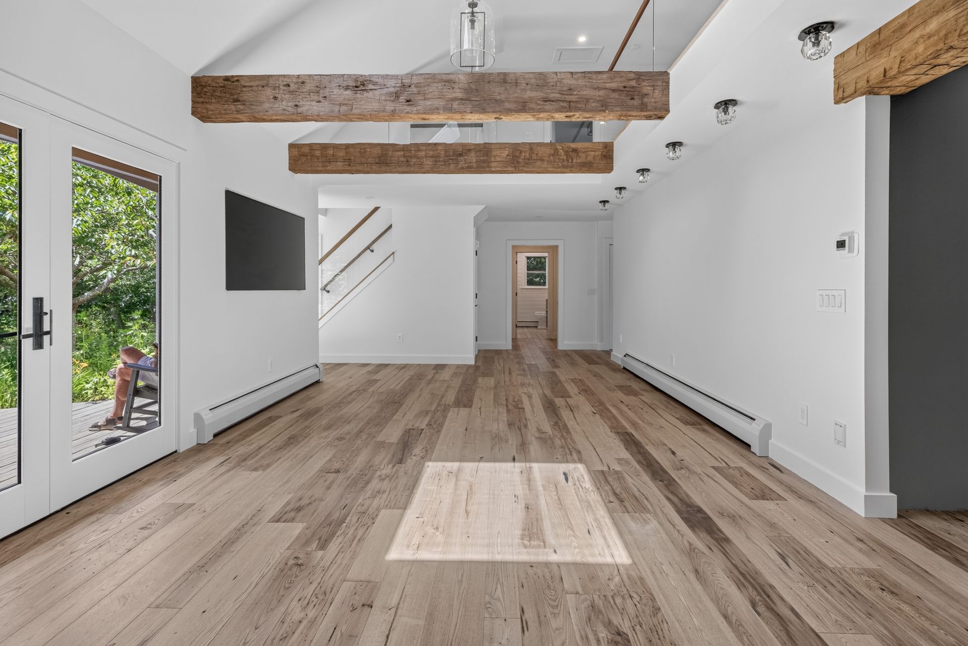 Bright modern open room with wood floors, white walls, exposed beams, and glass doors.