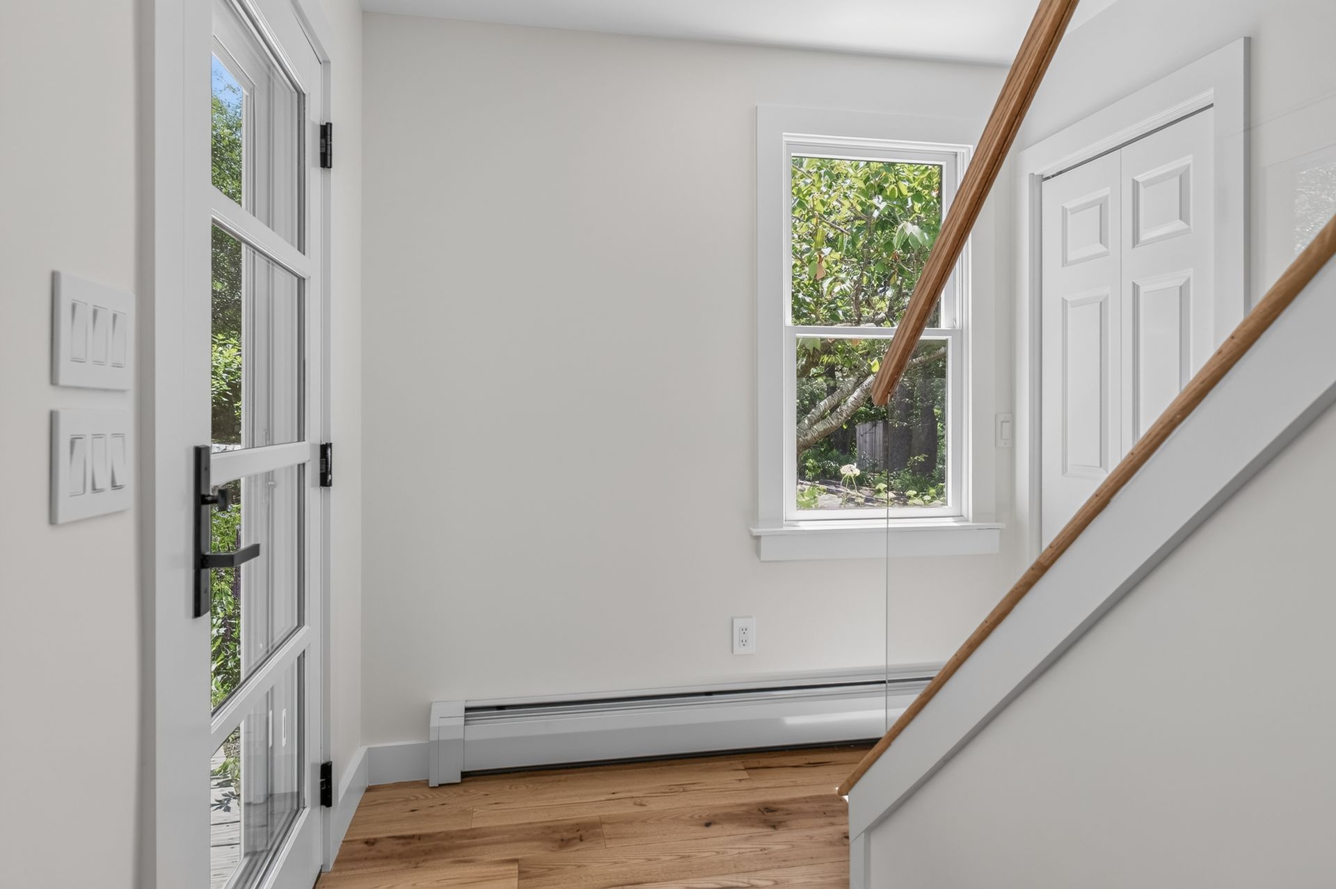 Bright entry hallway with white walls, wood floor, stairs, and a window by the front door