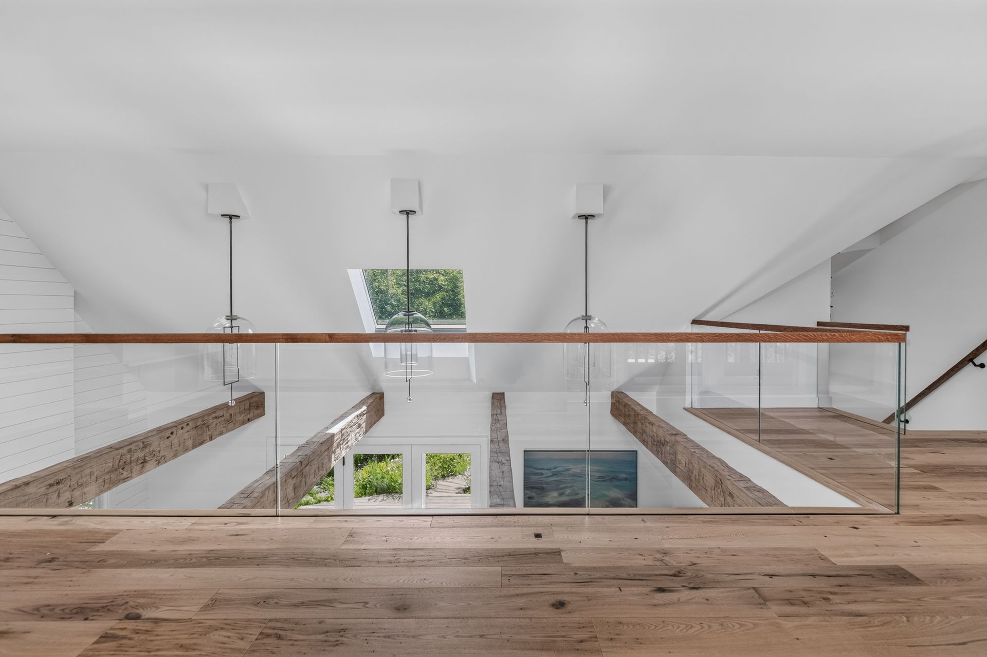 Loft balcony with glass railing overlooking a bright white interior and wooden floorboards