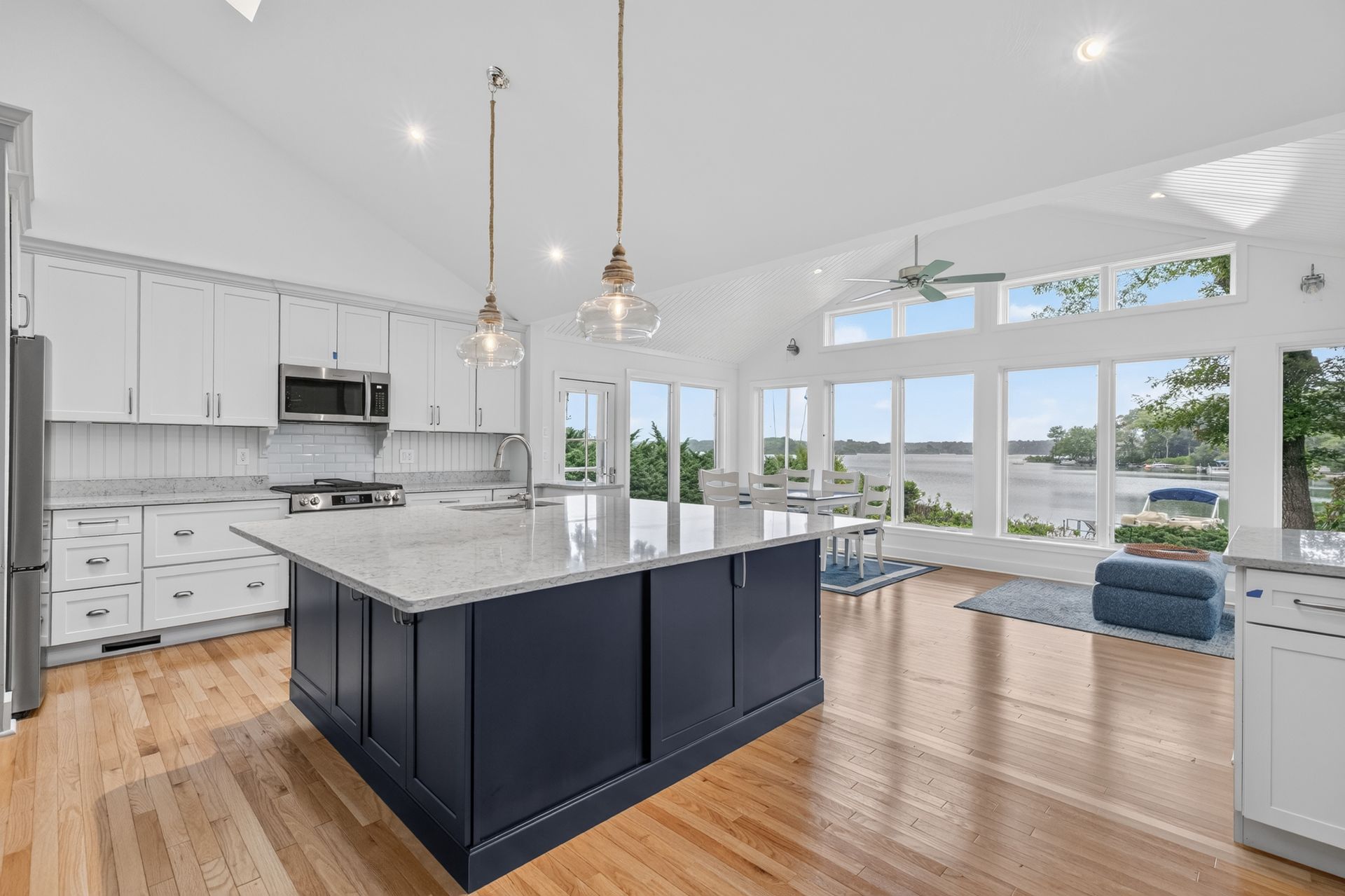 Bright modern kitchen with navy island, white cabinets, hardwood floors, and large windows overlooking a scenic view
