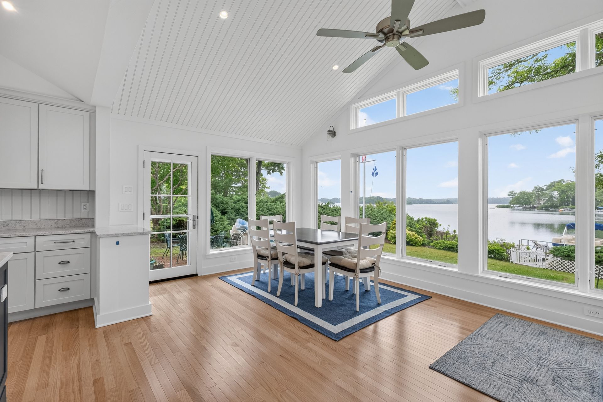 Bright dining area with large windows, white cabinets, wood floors, and a view of the water