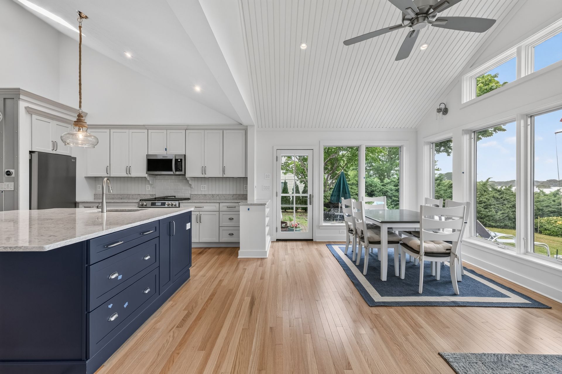 Bright open kitchen and dining area with white cabinets, blue island, wood floors, and large windows