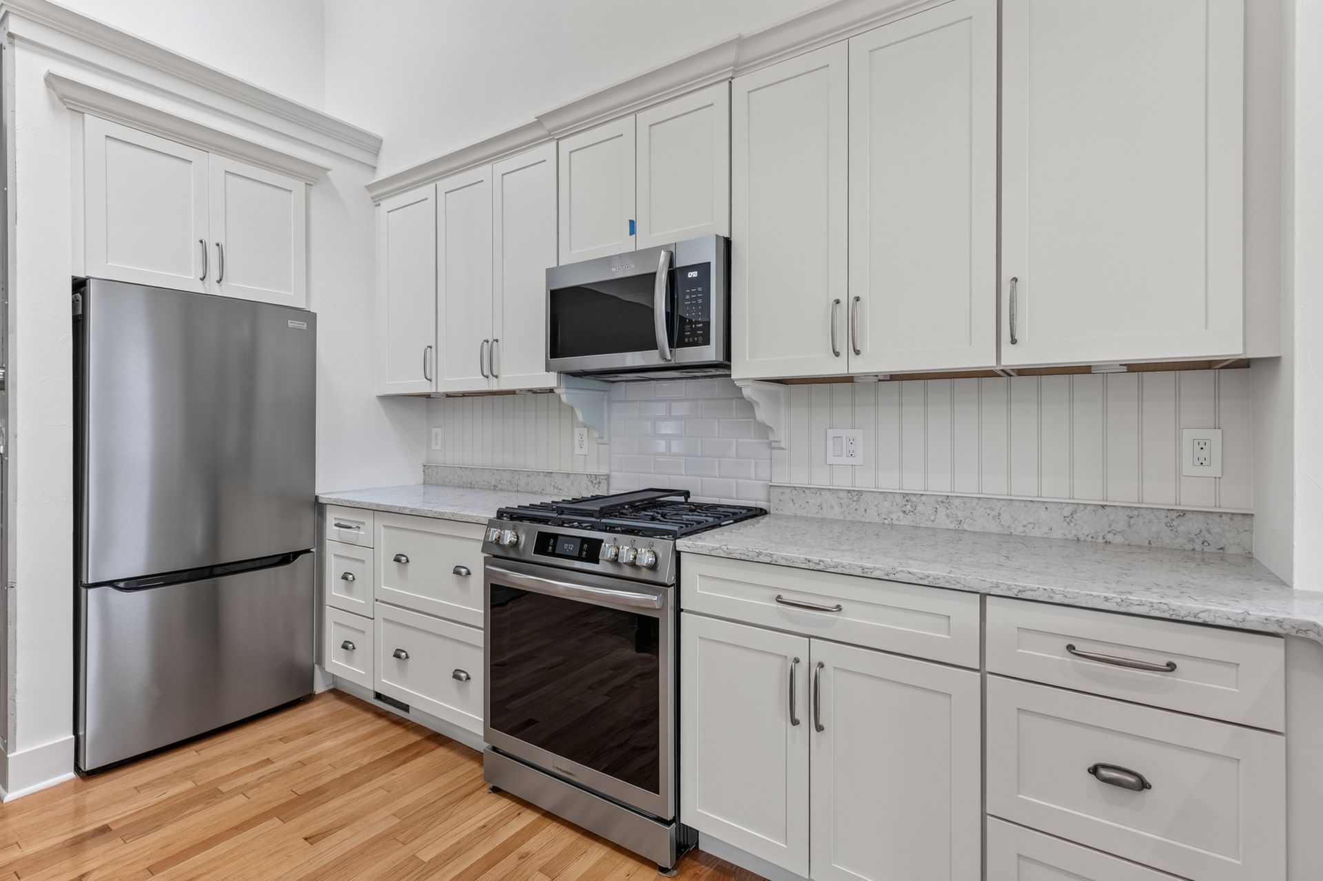 Bright modern white kitchen with stainless steel appliances, gray countertops, and wood floor