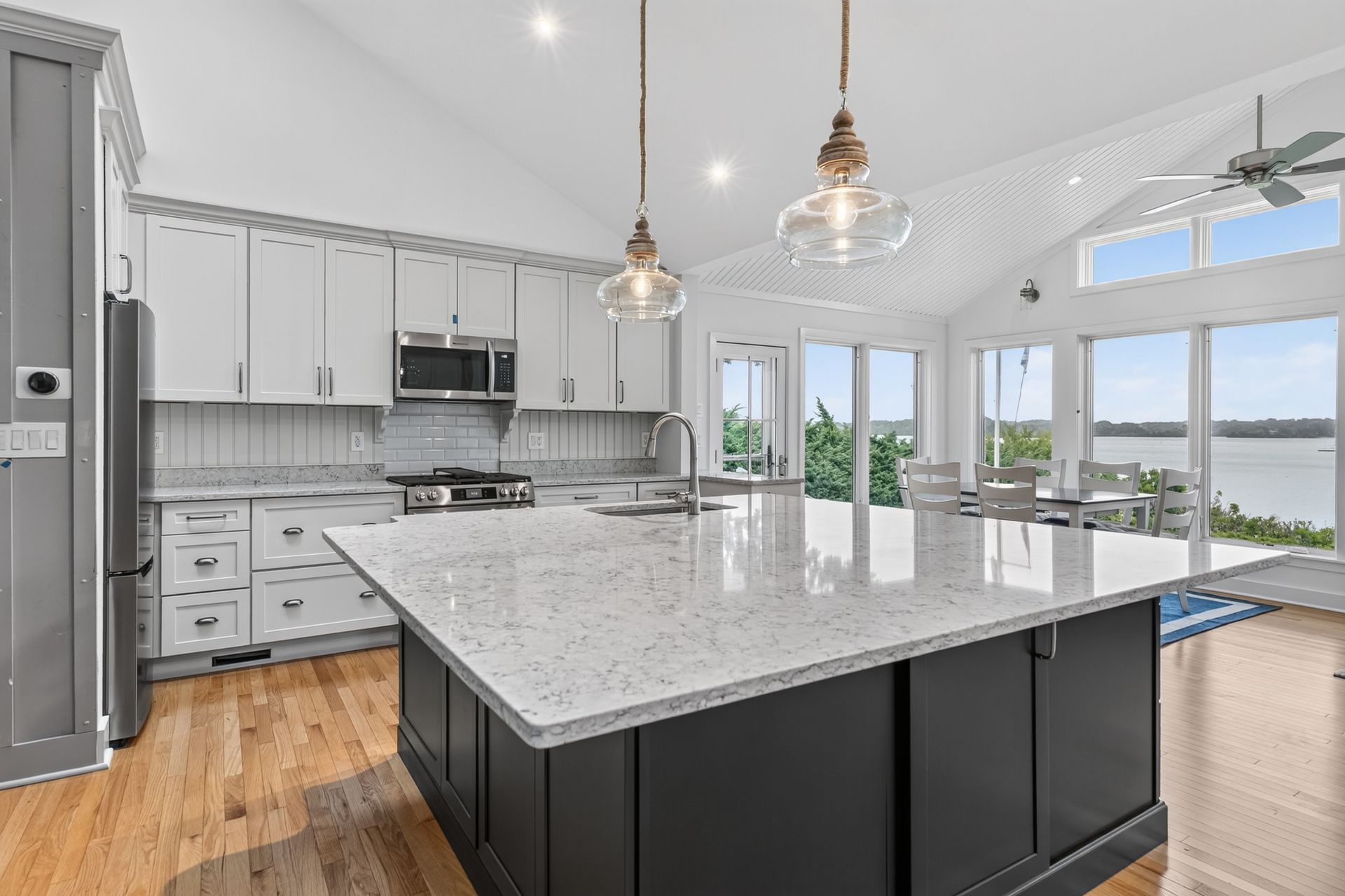 Bright modern kitchen with a large island, white cabinets, and pendant lights overlooking water.