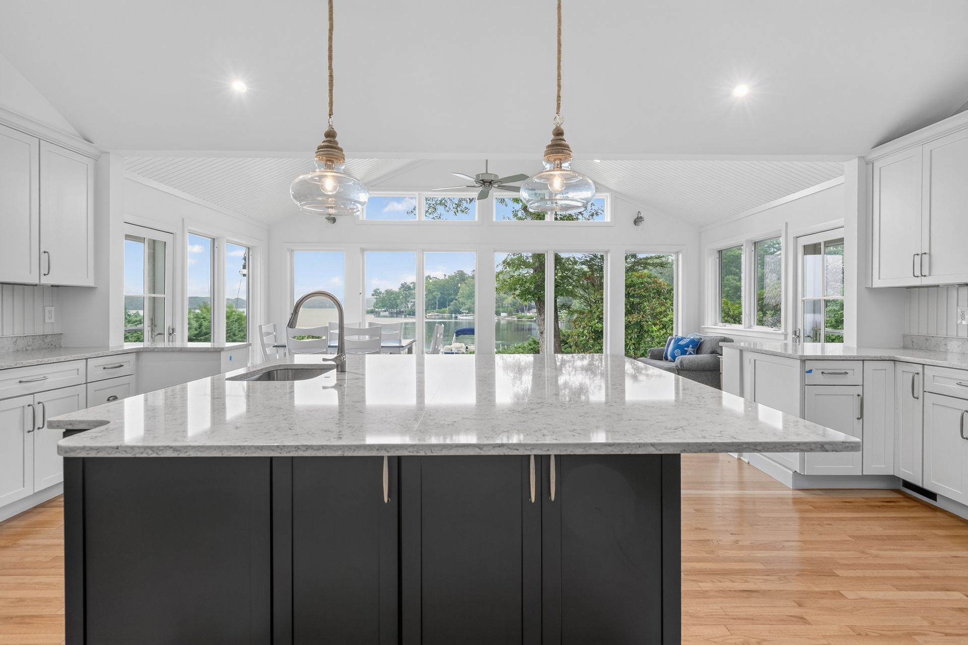 Bright white modern kitchen with large island, pendant lights, and wide windows overlooking greenery
