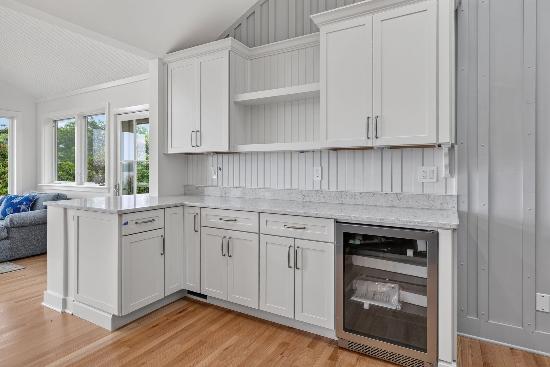 Bright white kitchen with shaker cabinets, marble backsplash, island, and wood floors