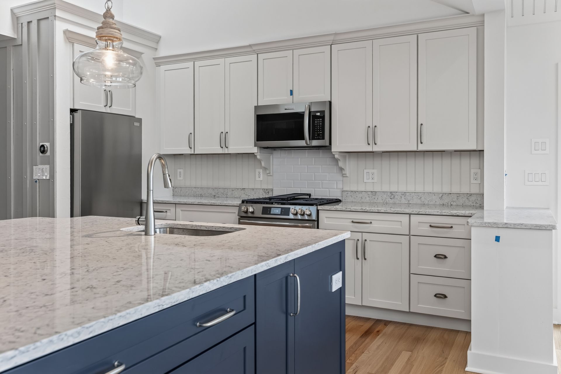 Modern white kitchen with blue island, granite counters, stainless appliances, and hardwood floor