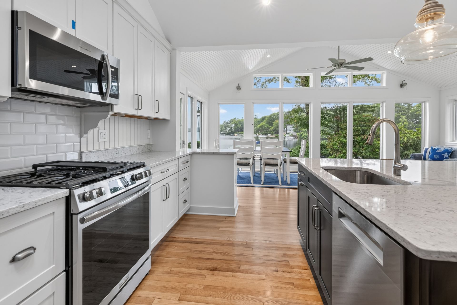 Bright modern kitchen with stainless appliances, white cabinets, marble island, and large windows overlooking greenery