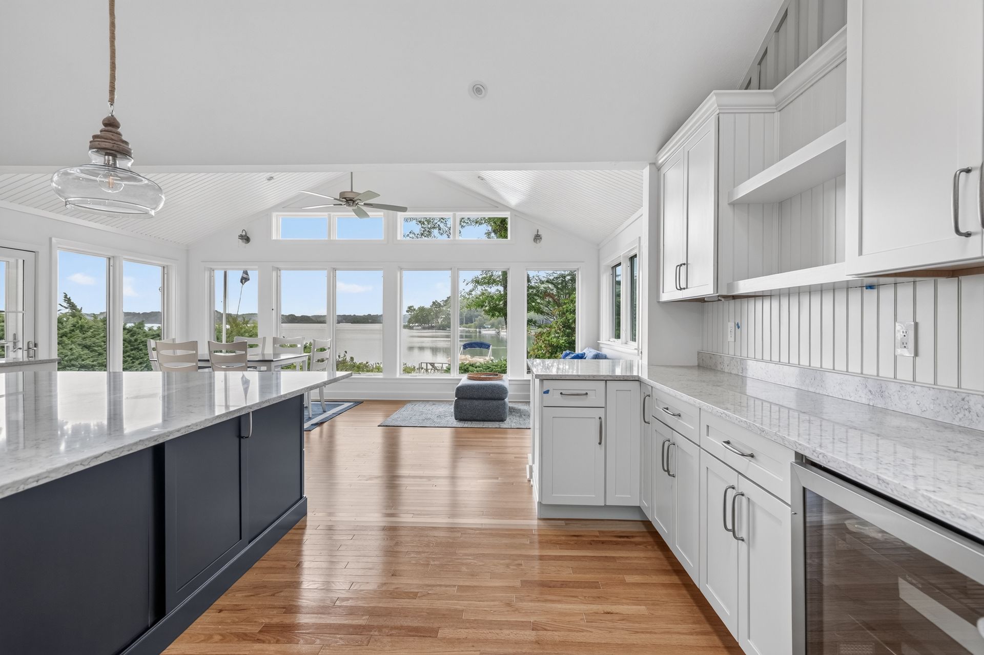 Bright modern kitchen with white cabinets, dark island, hardwood floors, and large windows overlooking water.